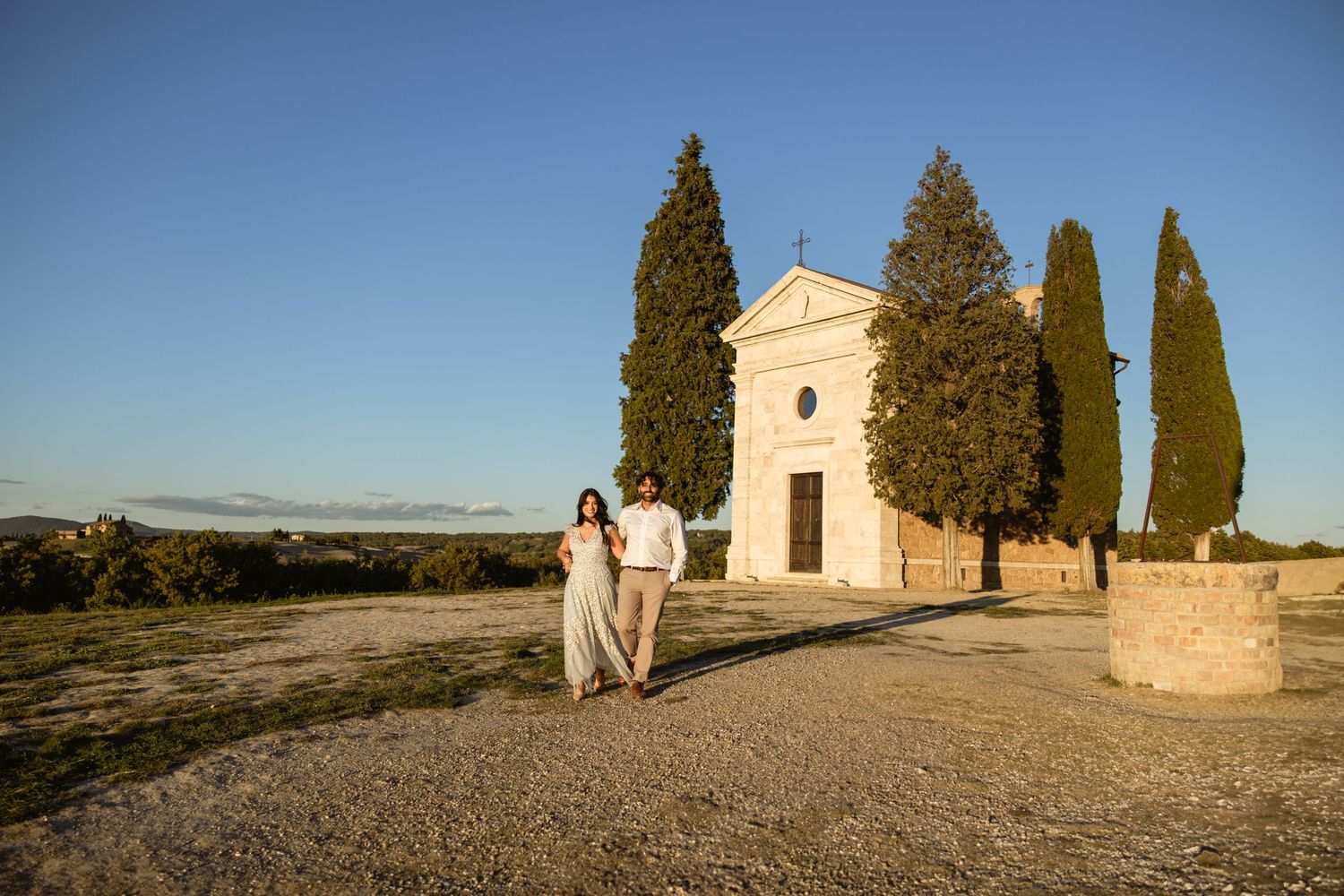 A rustic stone church with cypress trees stands against a clear blue sky in the Provence countryside.