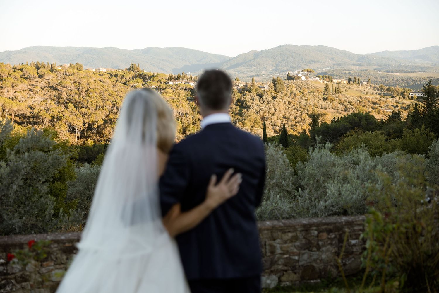 A couple embraces during sunset in the desert with mountains and cacti in the background.