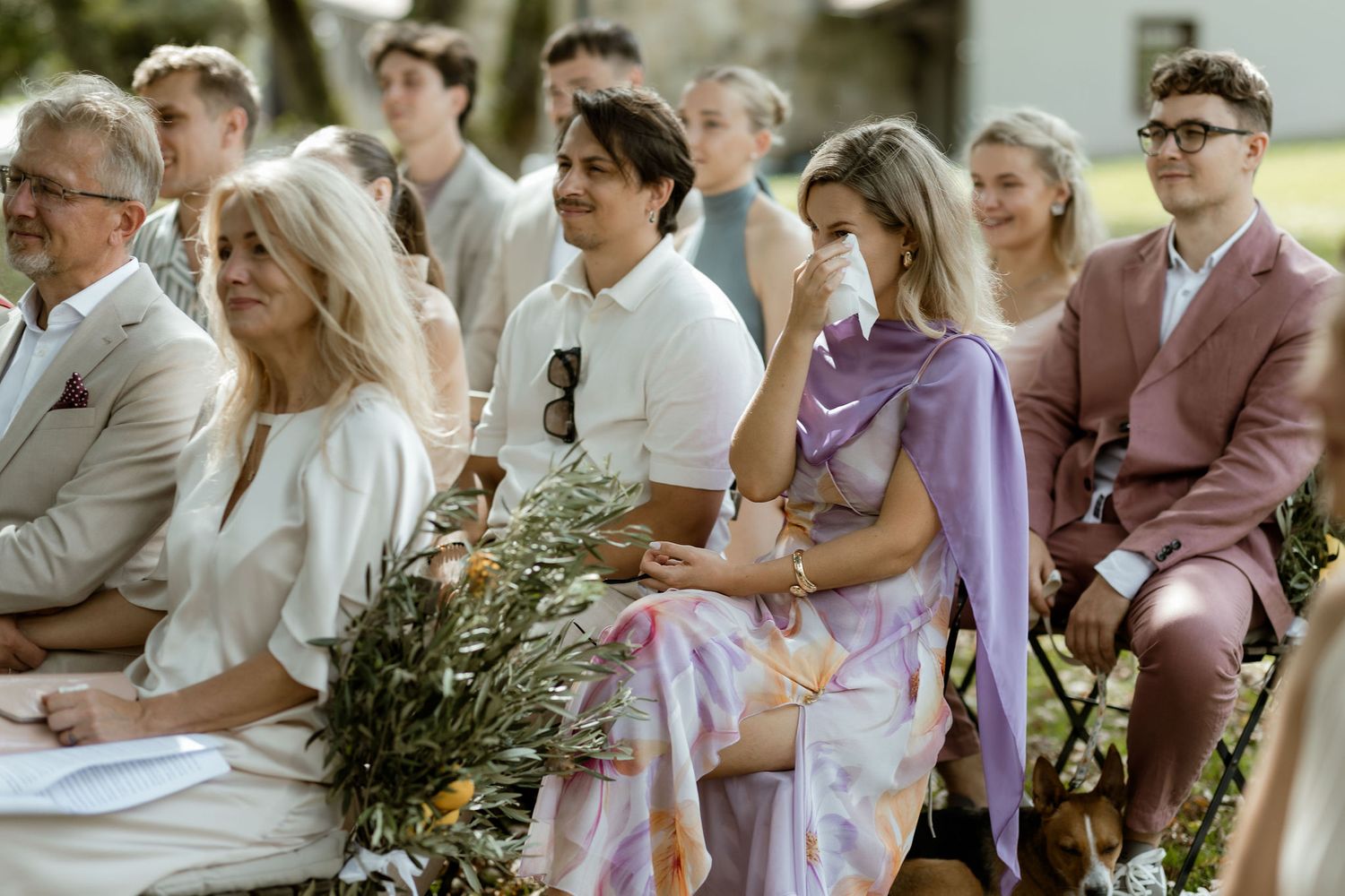 Wedding guests seated in rows outdoors watch an emotional ceremony unfold in a garden setting.