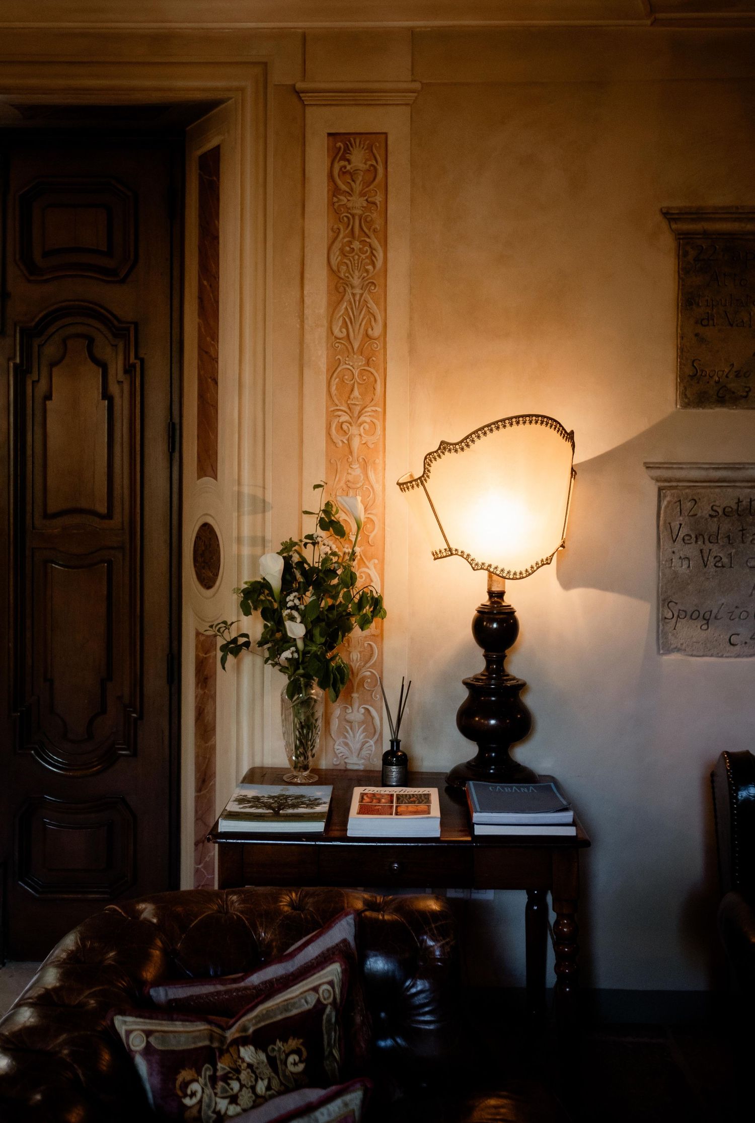 A vintage table lamp illuminates a cozy corner with wooden door, decorative molding and potted greenery on side table.