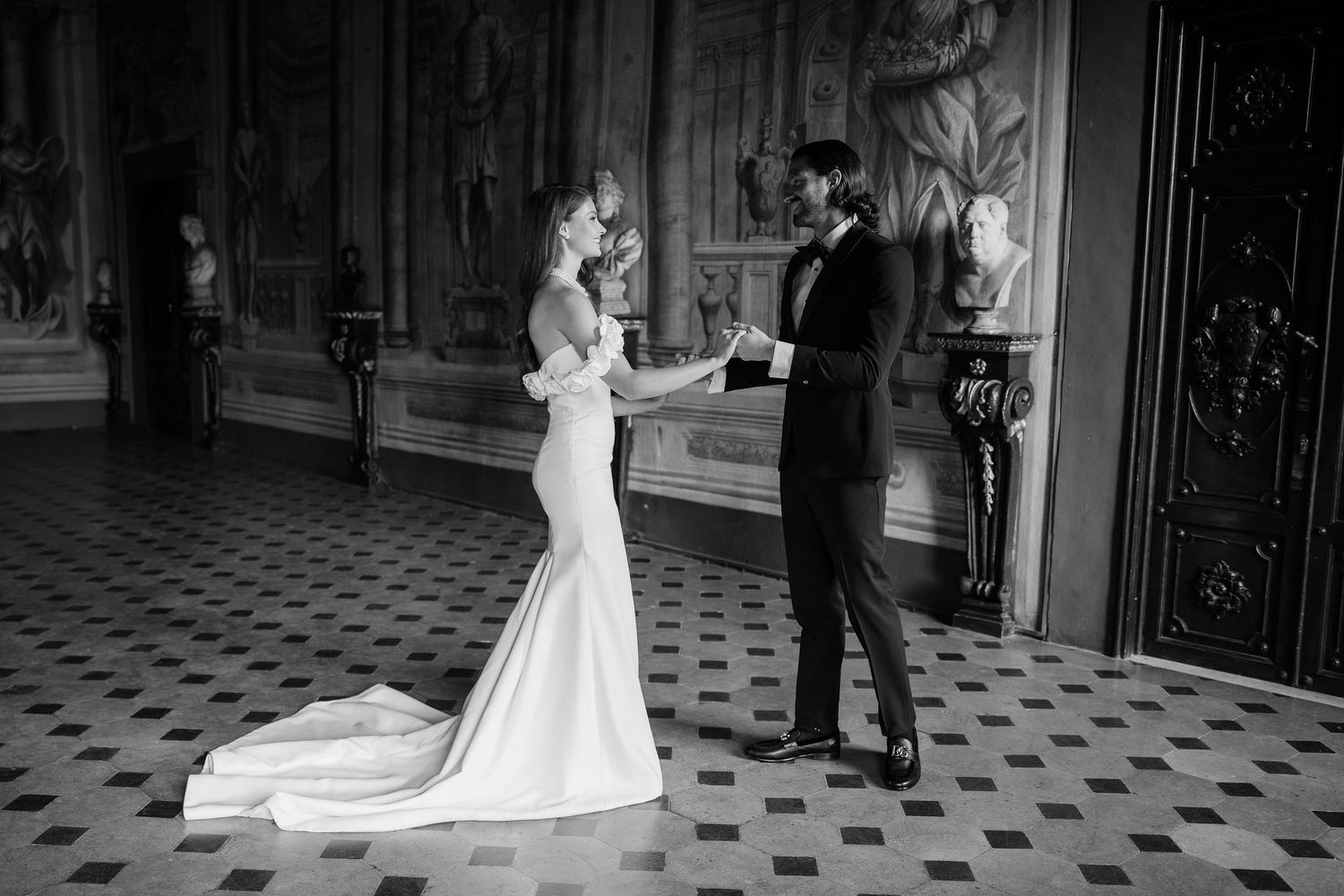 A bride and groom share a tender moment while dancing together in an elegant room with patterned floor tiles.