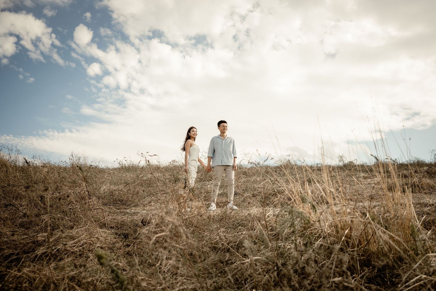 Couple standing on hilltop against cloudy sky in natural setting.