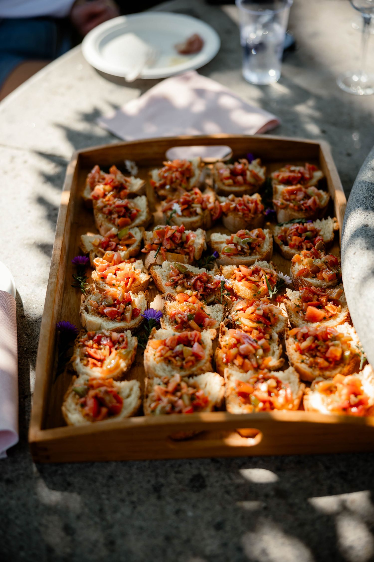 Wooden tray of gourmet appetizers served at outdoor catering event.