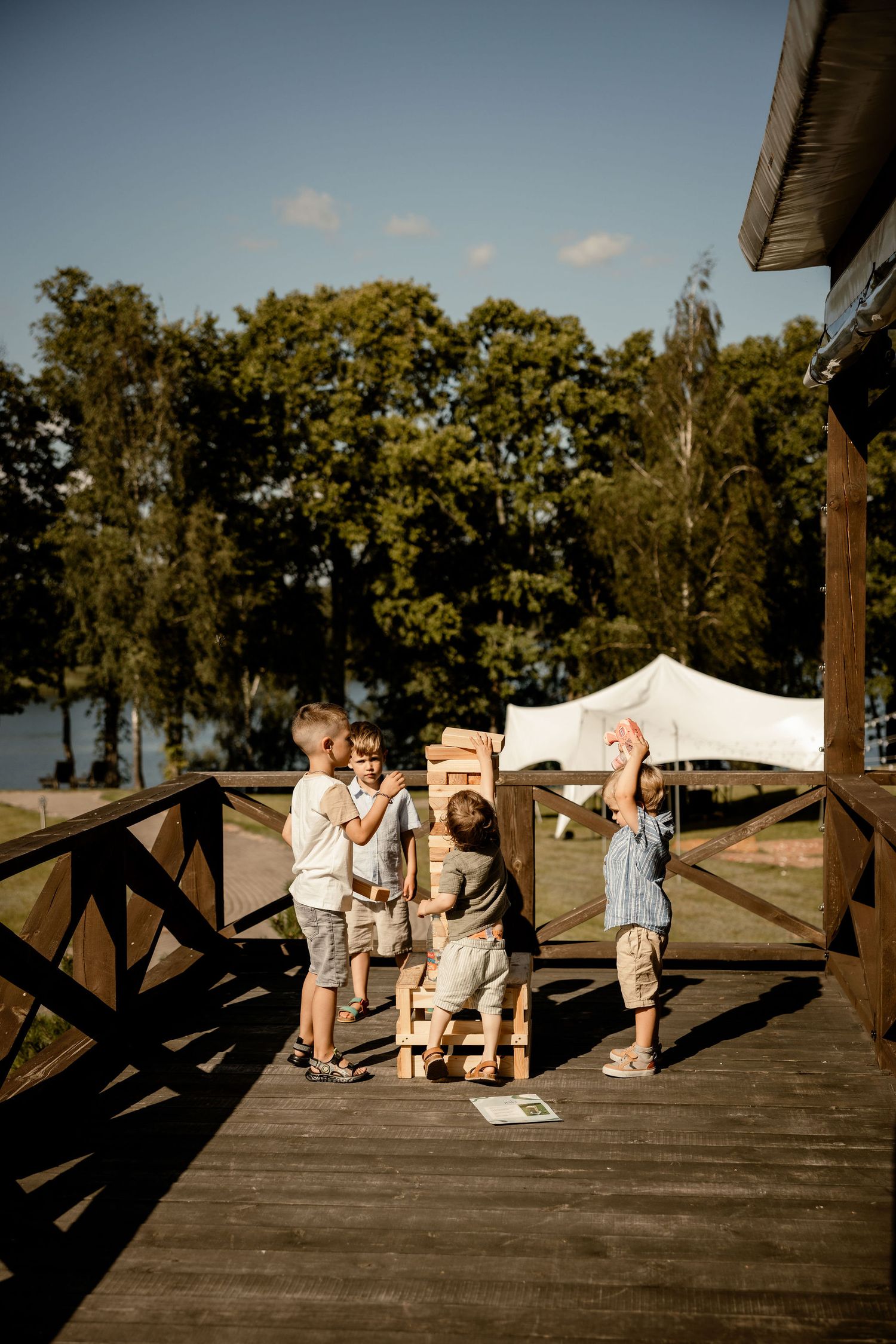 Children playing together on a wooden deck overlooking a lakeside setting.