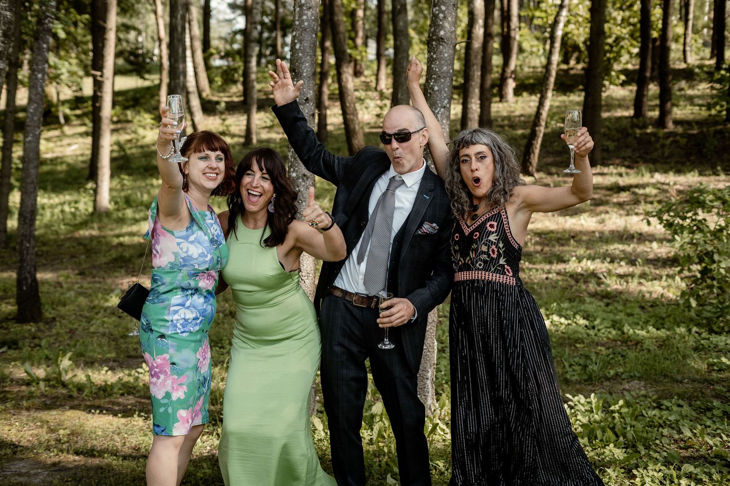Group celebrates joyfully in sunlit forest setting during wedding festivities.