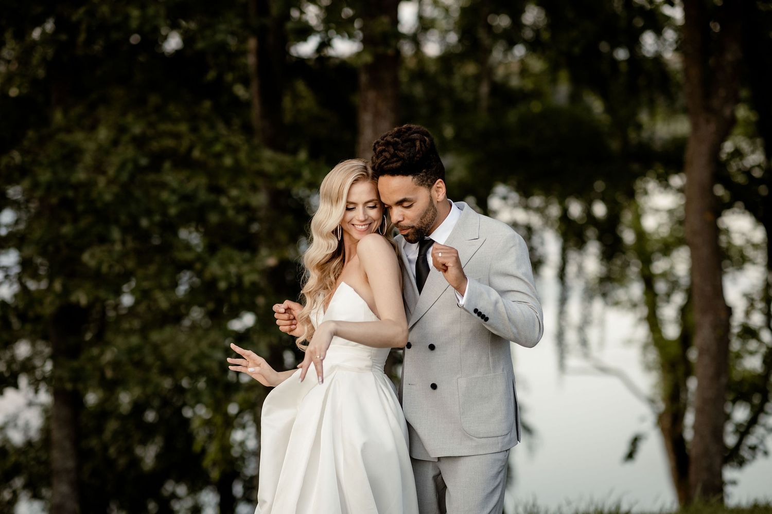 A romantic couple in wedding attire embrace outdoors surrounded by lush trees on their special day.