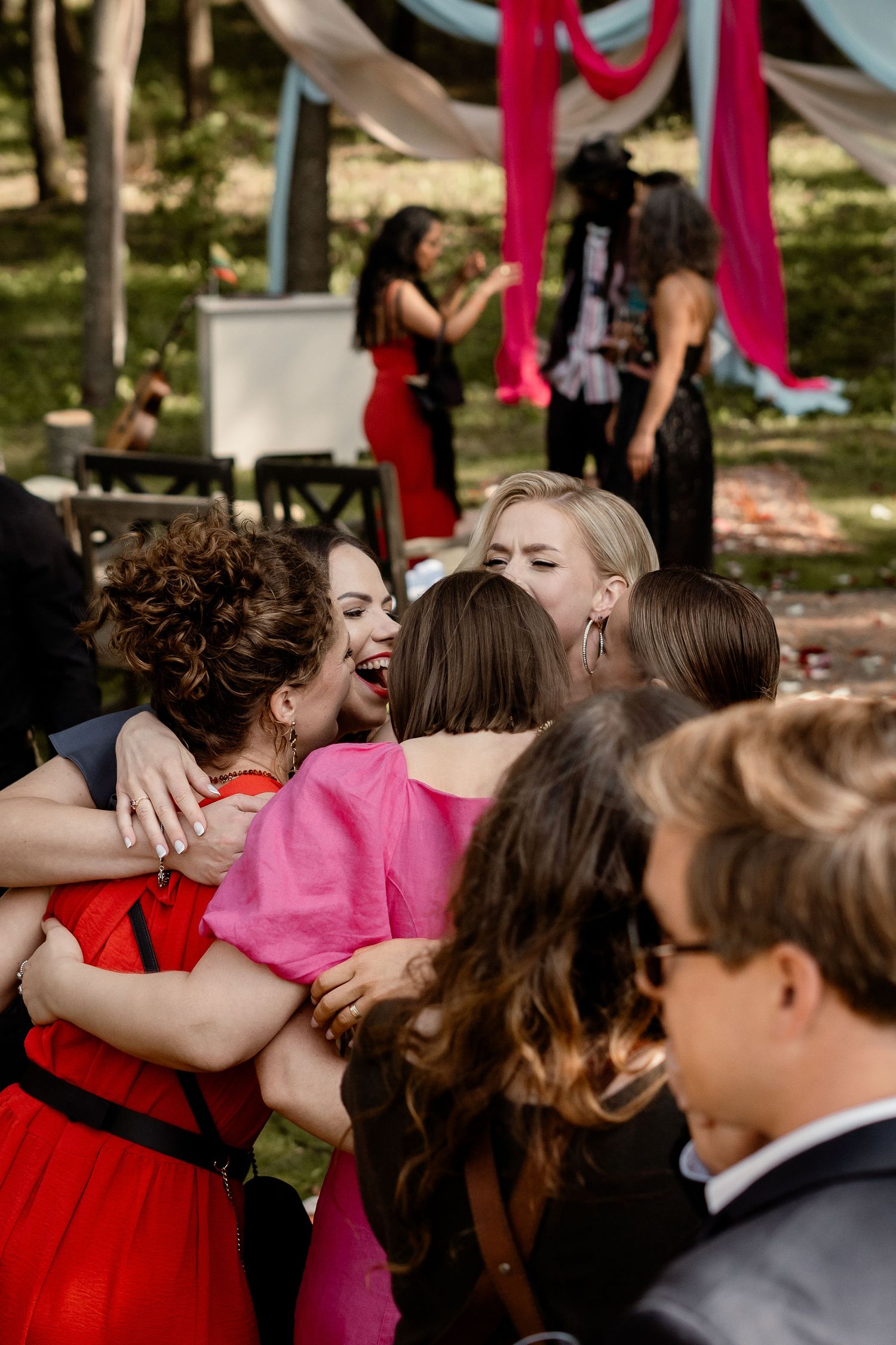 Group of wedding guests sharing laughter and hugs during outdoor celebration.