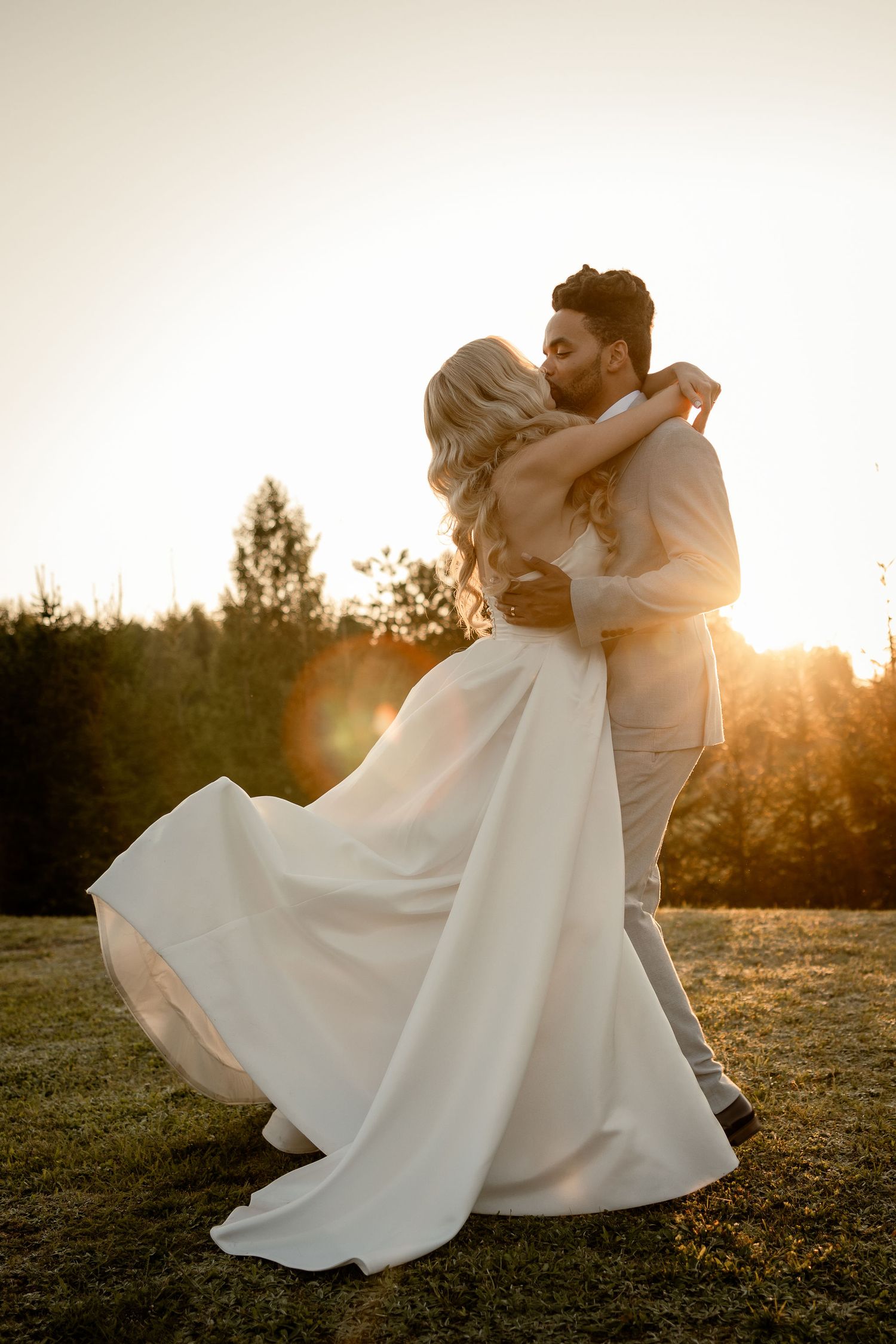 A romantic outdoor wedding photo shows a couple embracing in golden sunset light as the bride's white dress flows in the breeze.