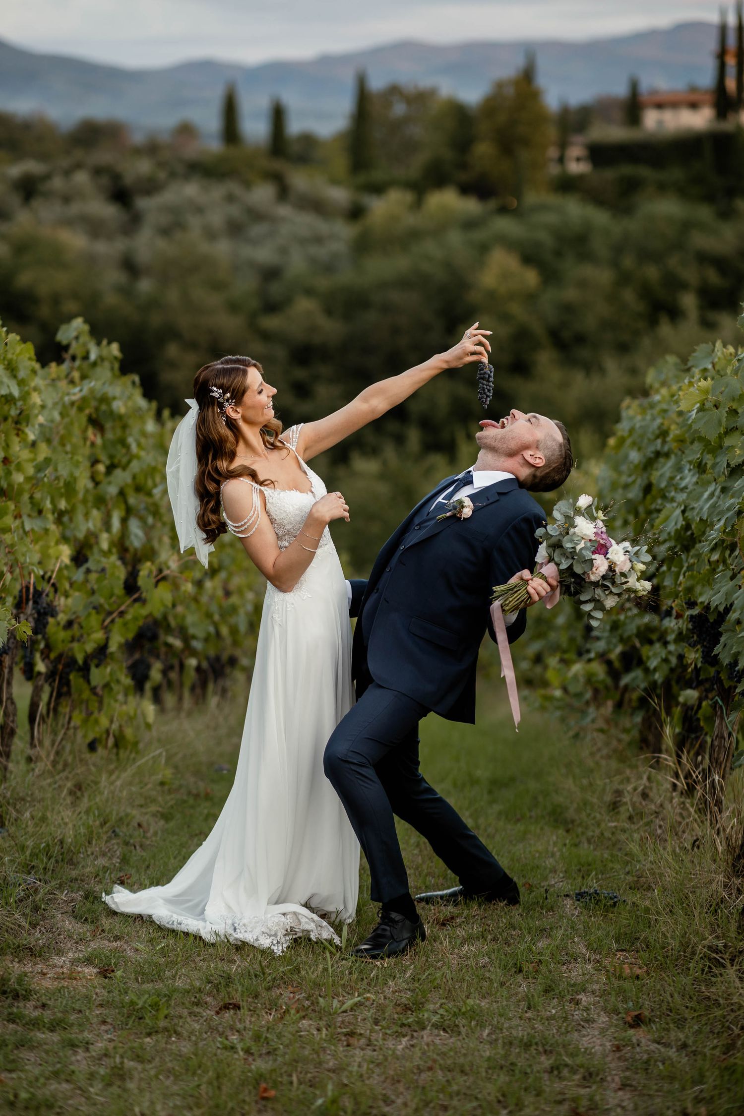 Couple shares a fun moment in vineyard with dramatic poses and mountain views.
