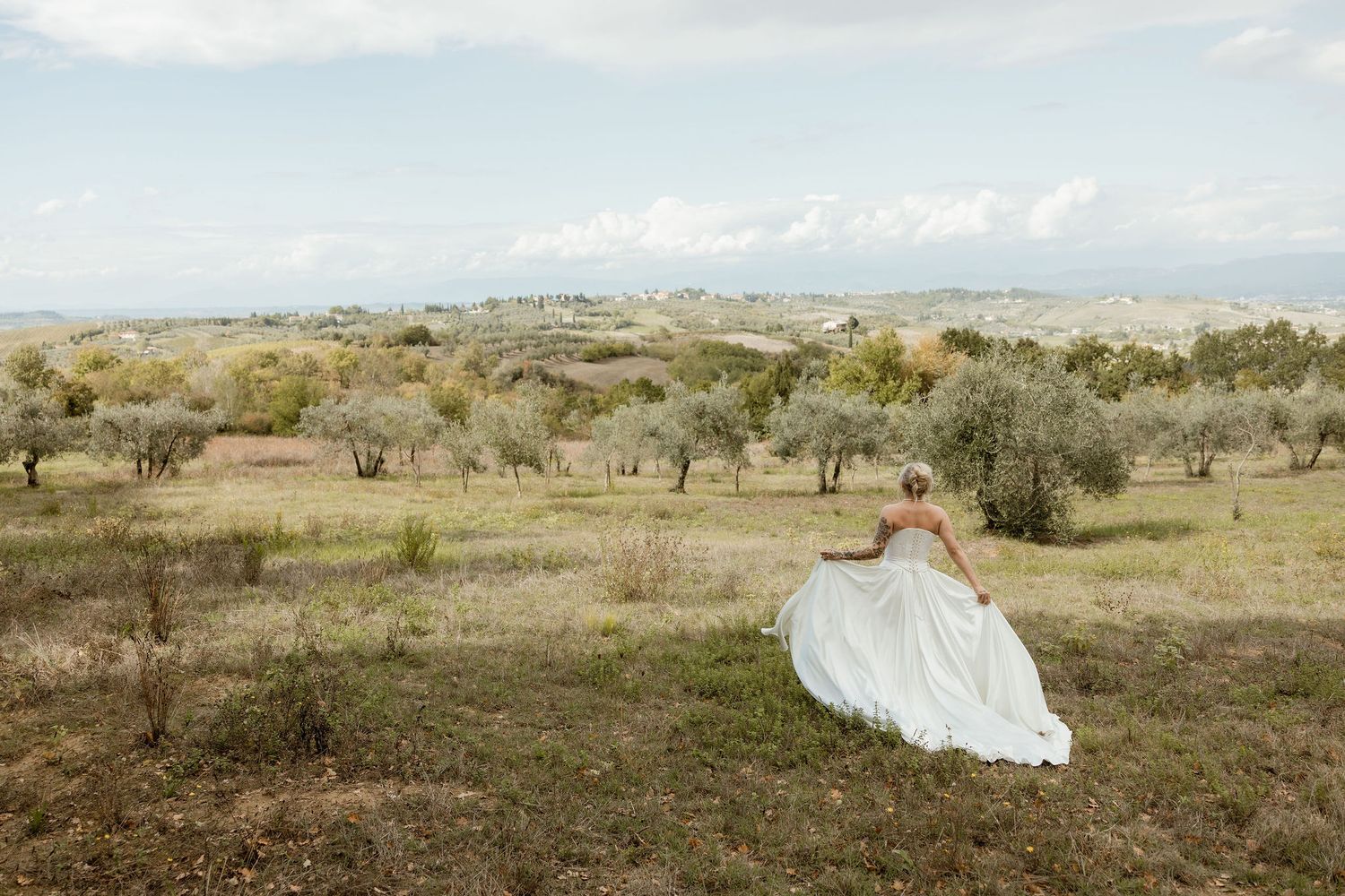 A bride in a flowing white dress runs through a desert landscape surrounded by sagebrush and golden hills.