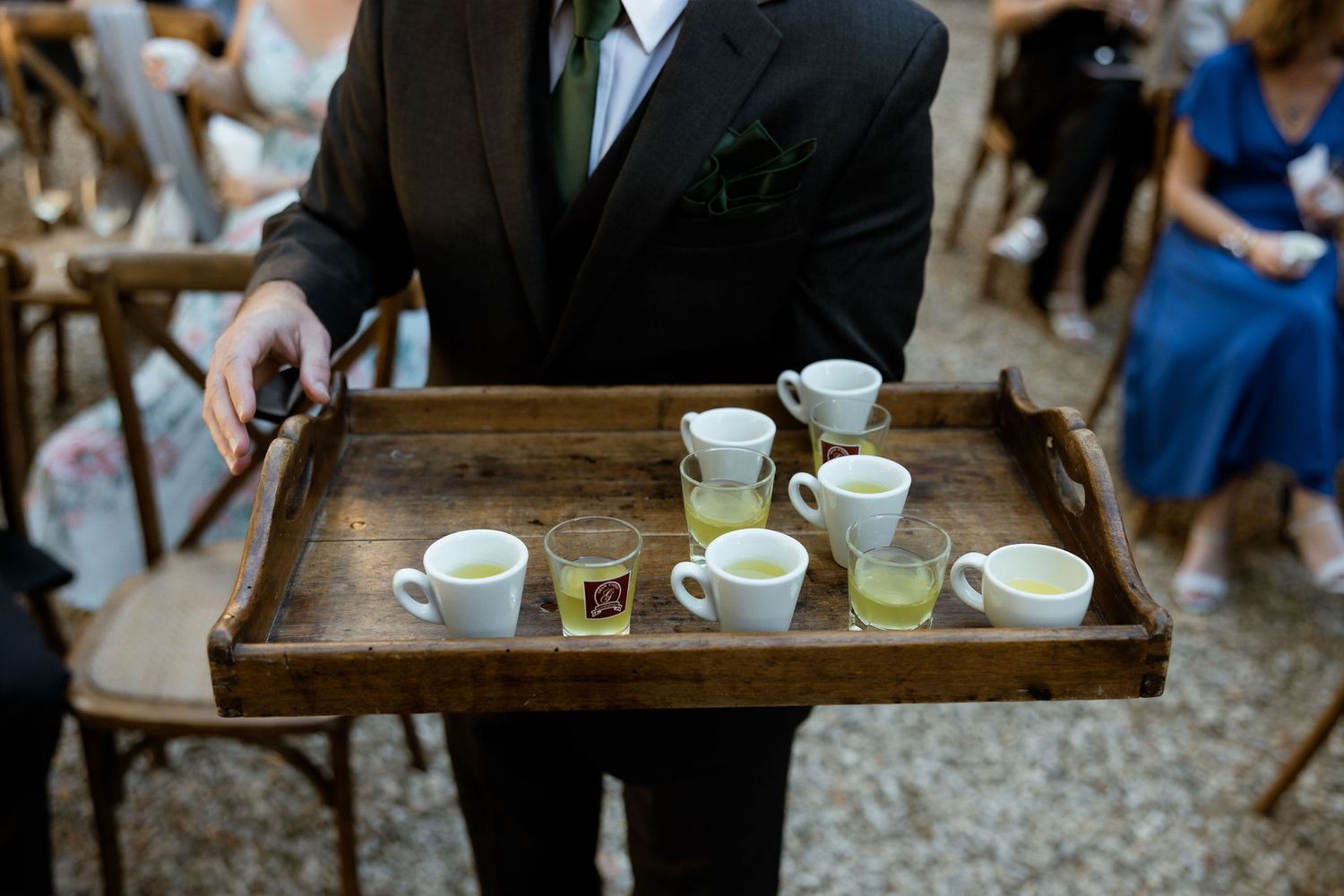 Wedding guests enjoy refreshments and appetizers served on rustic wooden trays at an outdoor reception.