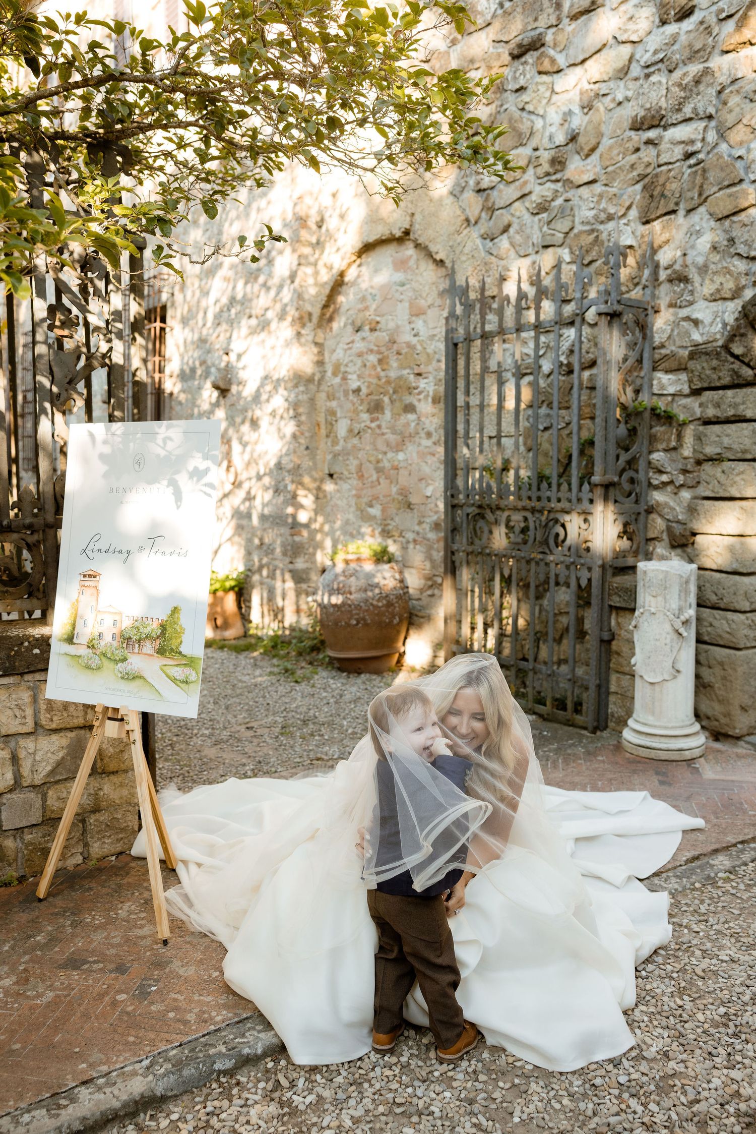 A romantic wedding moment captured in a rustic stone courtyard with iron gates and dappled sunlight.