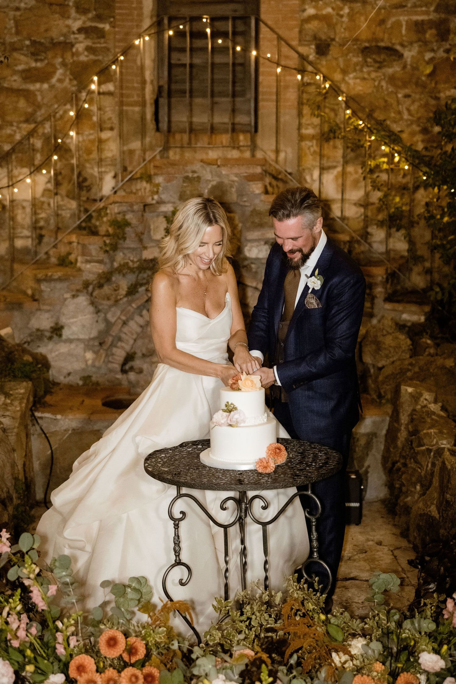 A romantic wedding couple shares intimate moments on a rustic stone bench surrounded by floral decorations.