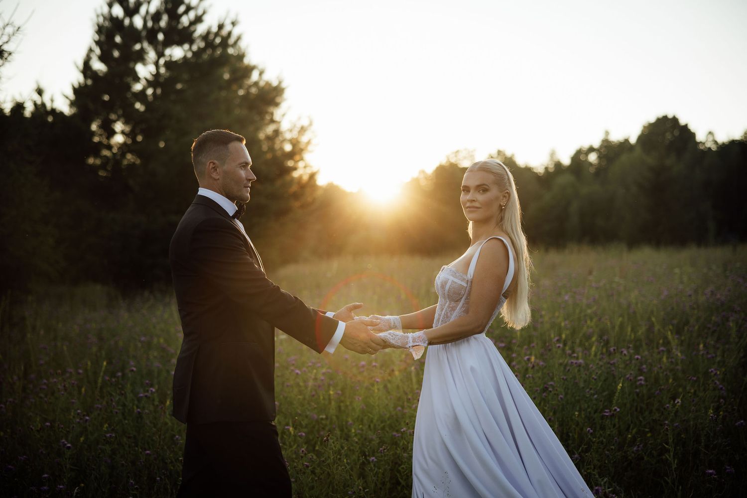 Romantic sunset wedding photo of couple holding hands in a wildflower meadow with glowing golden light.