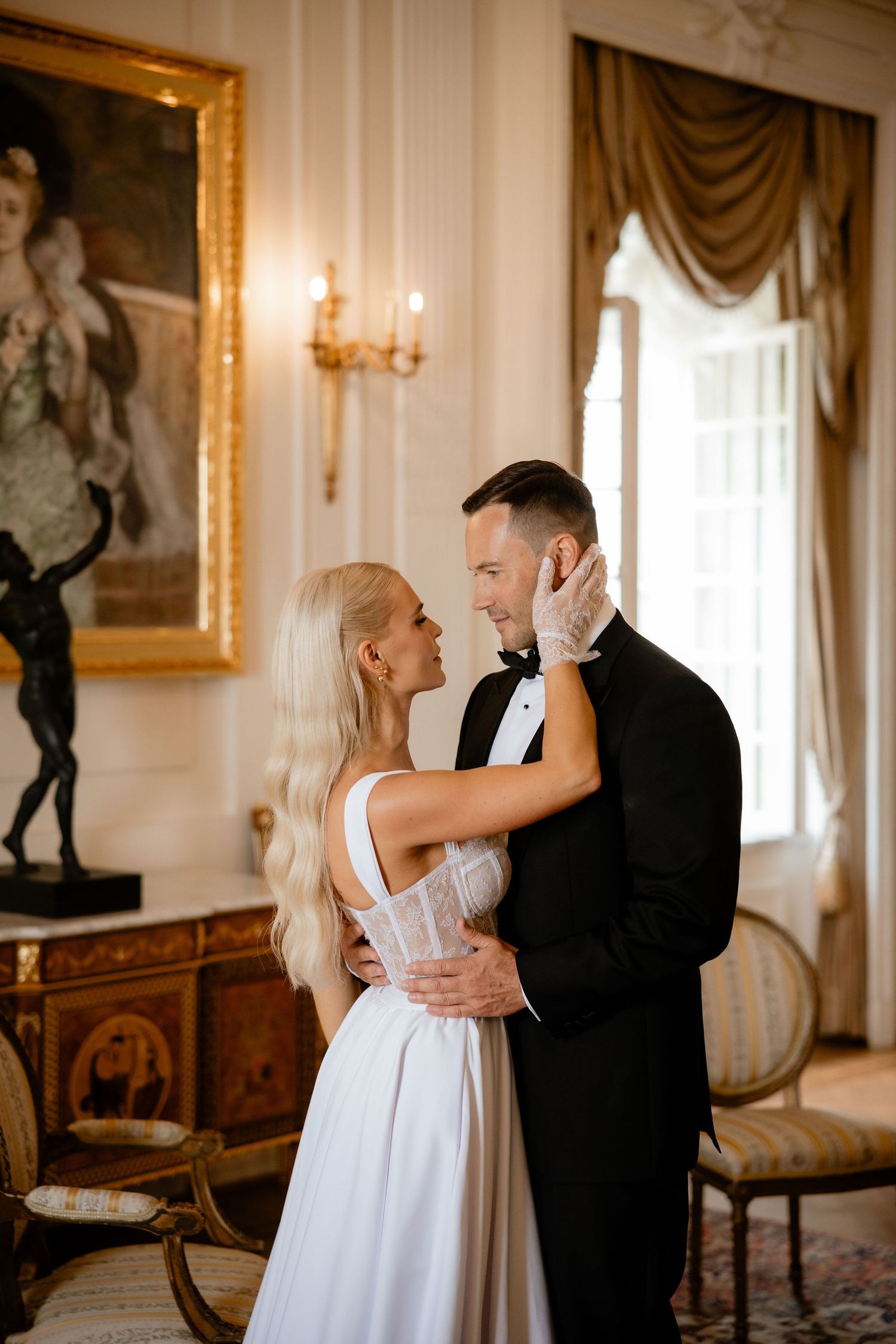 Couple embracing in formal wear against backdrop of classic interior with gilded frames.