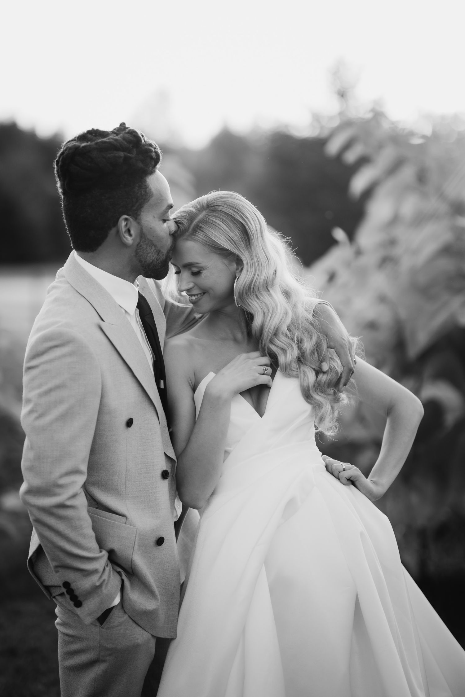 A romantic black and white wedding portrait of a couple sharing an intimate moment outdoors.