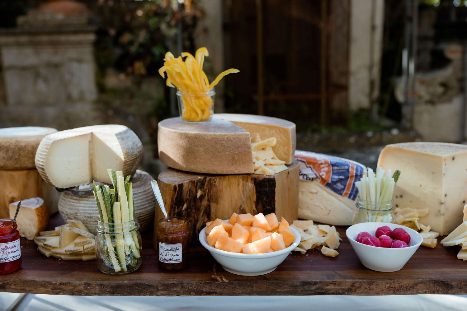 A rustic wooden table displays an appetizing cheese board with fresh vegetables, bowls of radishes and cantaloupe.