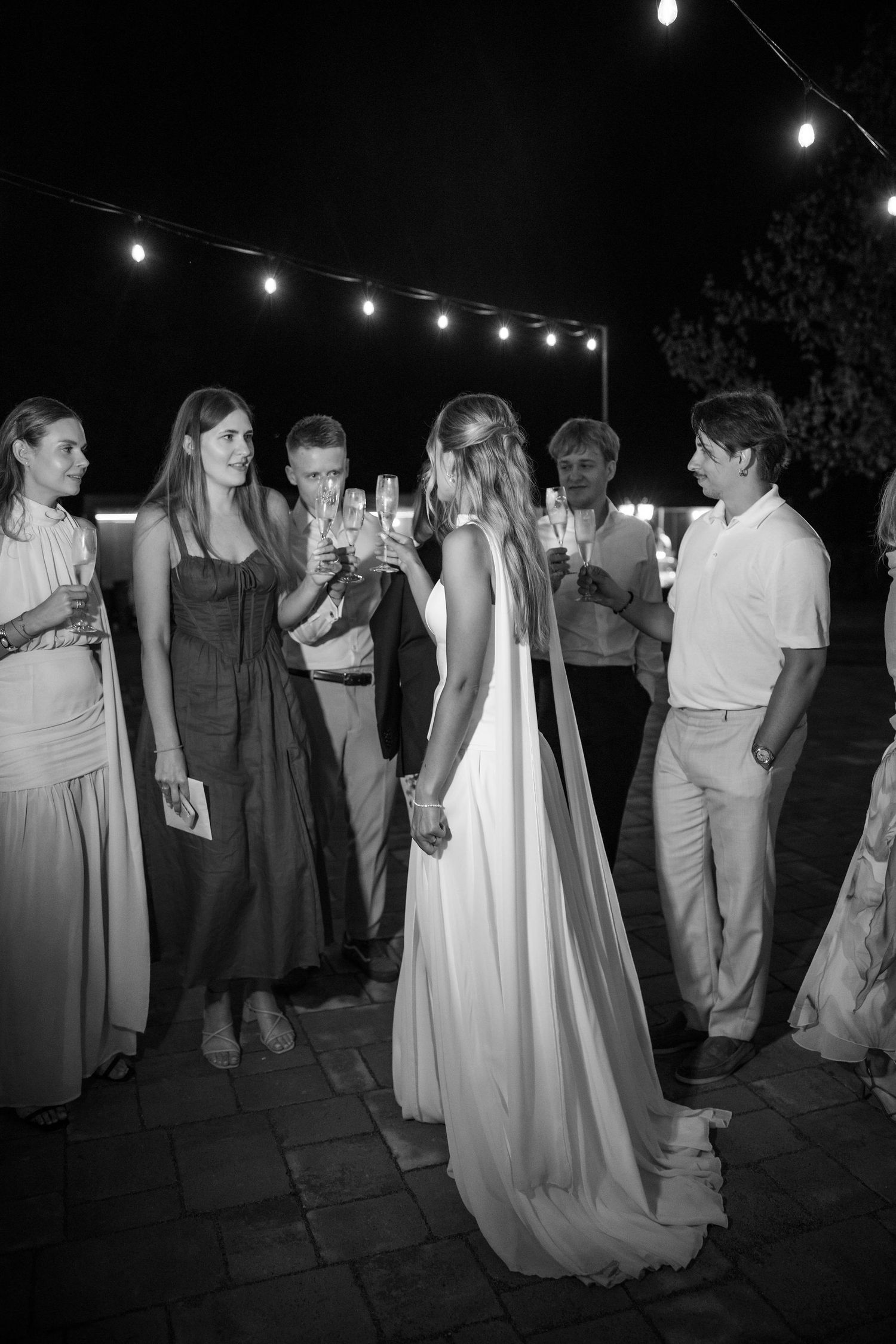 Wedding guests dance under twinkling string lights at an outdoor evening reception in black and white photography.