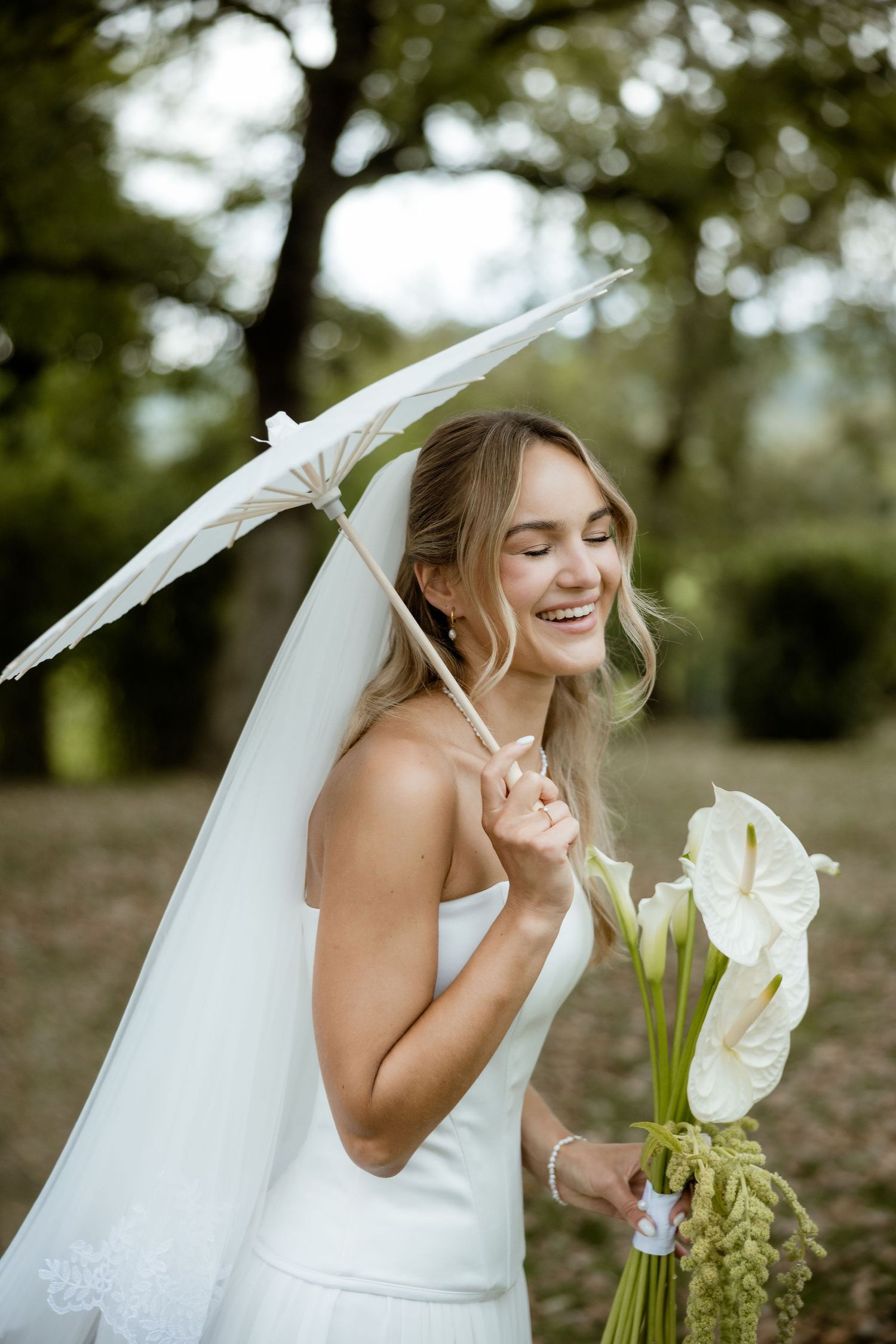 A bride in a white wedding dress poses with calla lily flowers in an outdoor garden setting.