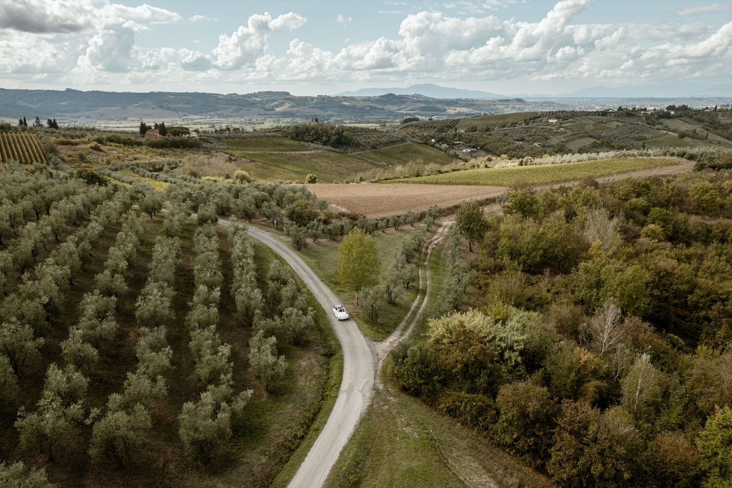 Winding mountain road curves through scenic rolling hills and green landscape with mountains in the distance.