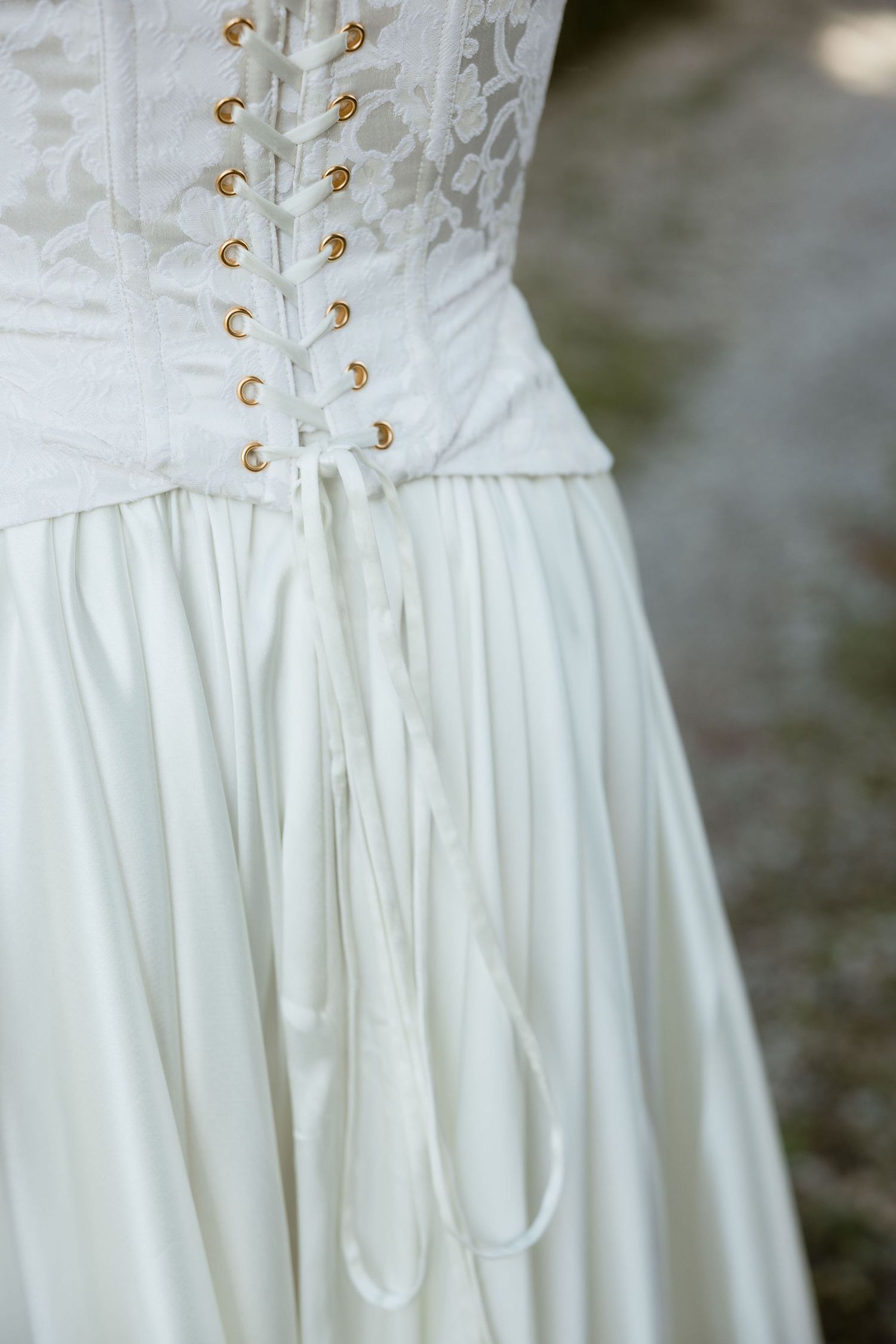 Close-up detail of a white corset dress with gold lace-up eyelets showing delicate craftsmanship and texture.