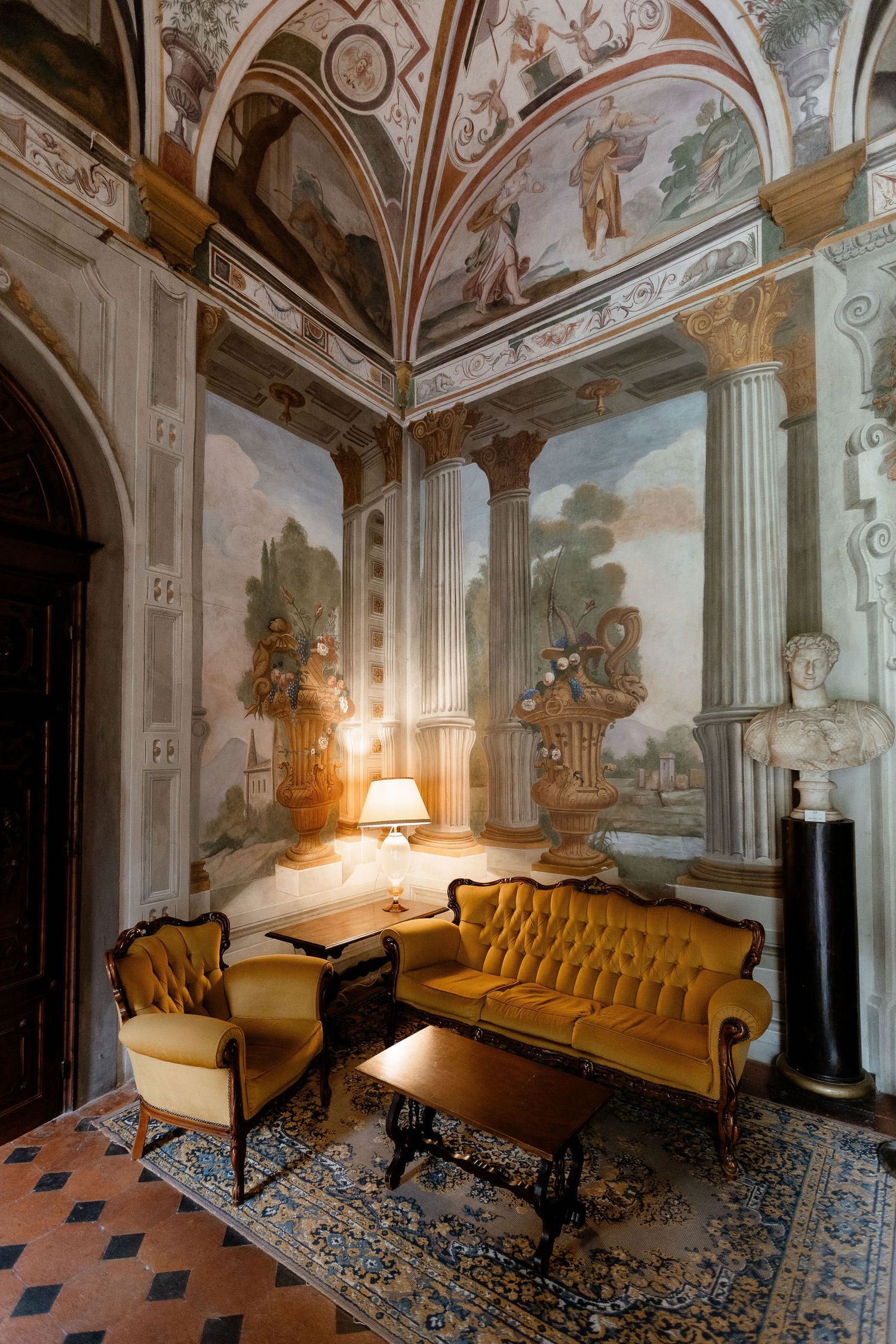 Opulent baroque room with frescoed walls and ceiling, featuring antique gold furniture and a patterned rug illuminated by lamplight.