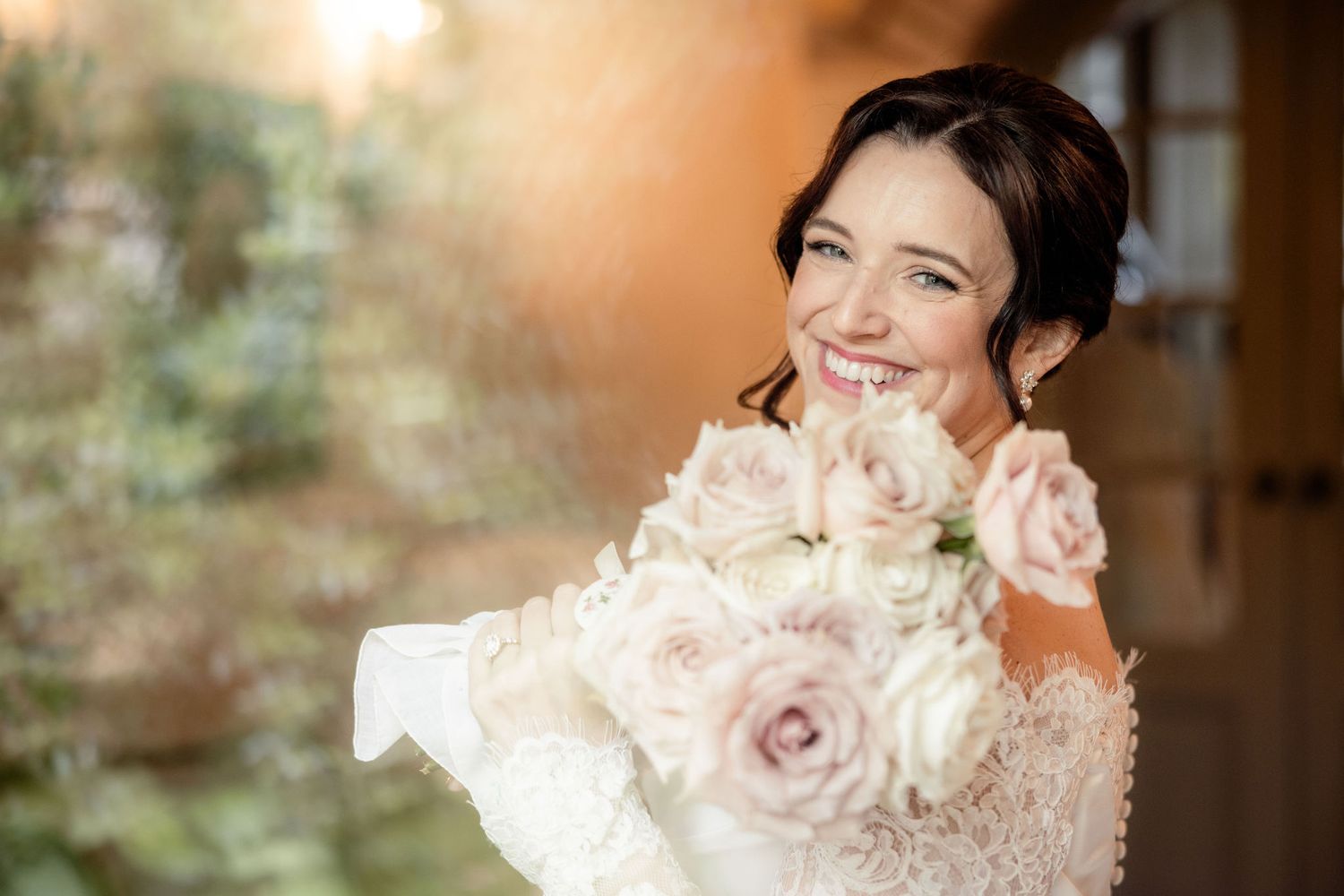 Bride holds beautiful blush pink and white rose bouquet while wearing delicate lace wedding dress.