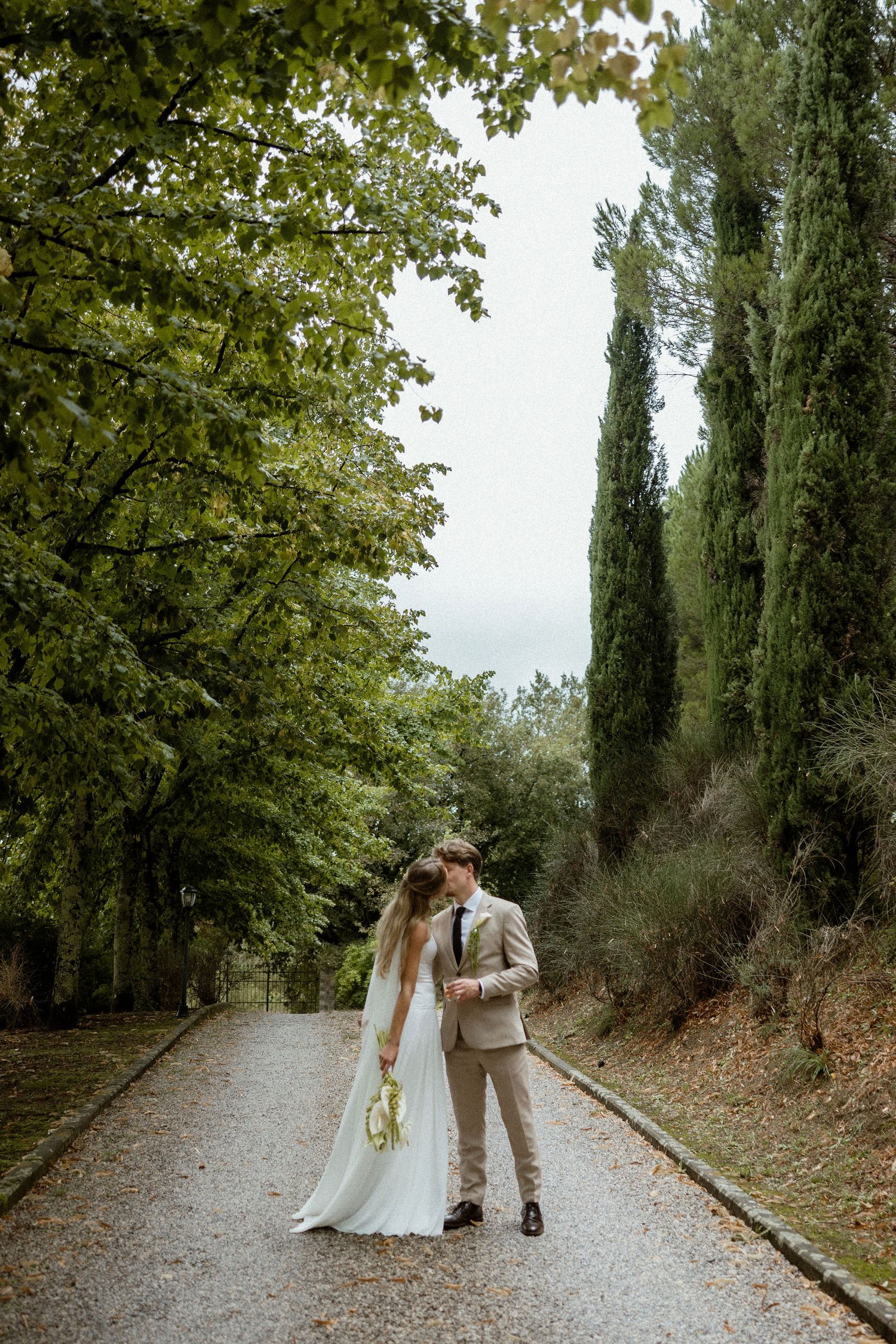 A couple shares romantic moments along a tree-lined pathway in a rustic outdoor setting.