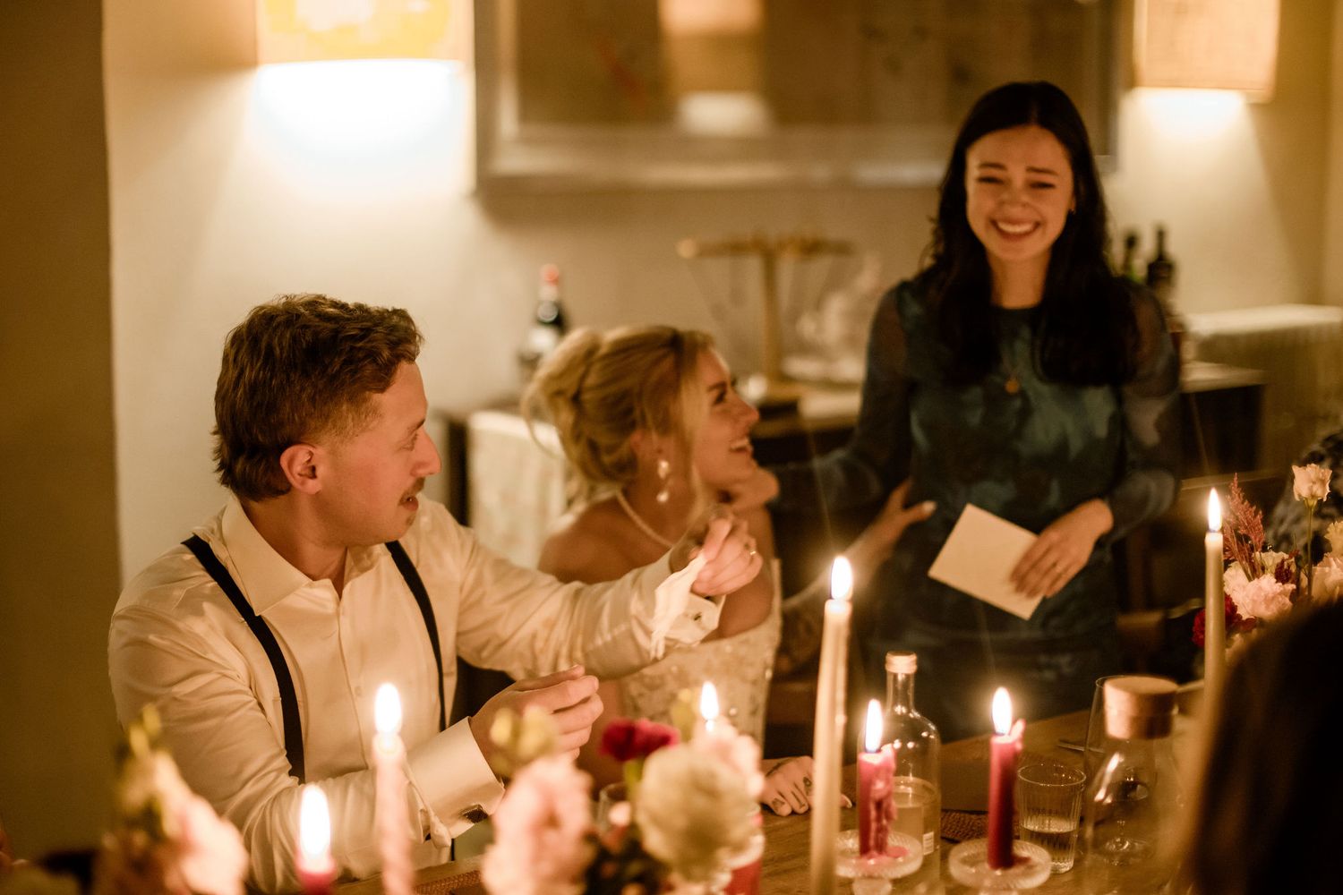 Candlelit dinner party scene with guests seated at a long table in a warm, intimate setting.