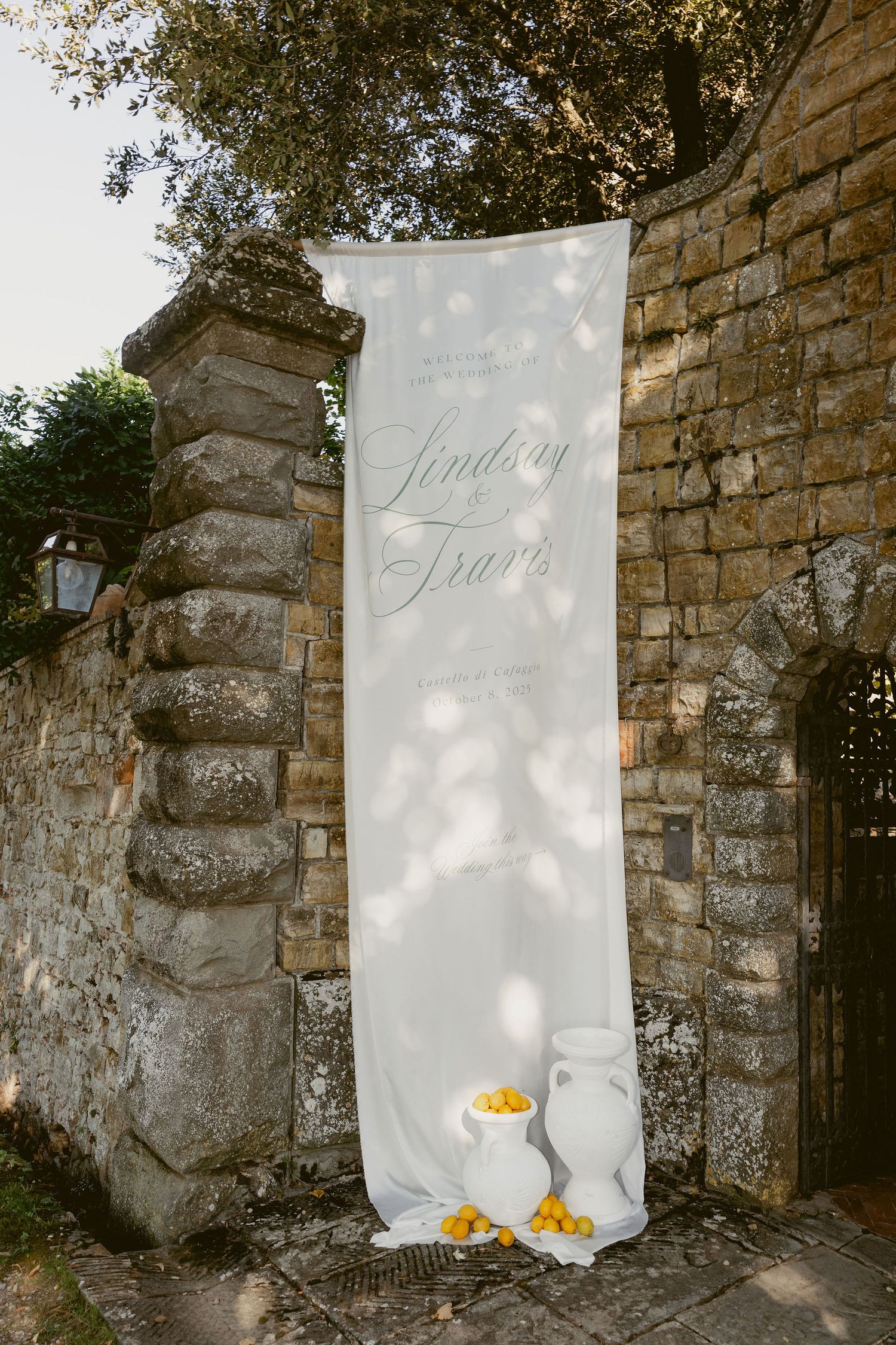 White fabric banners with yellow flowers hang against rustic stone walls in an outdoor garden setting.