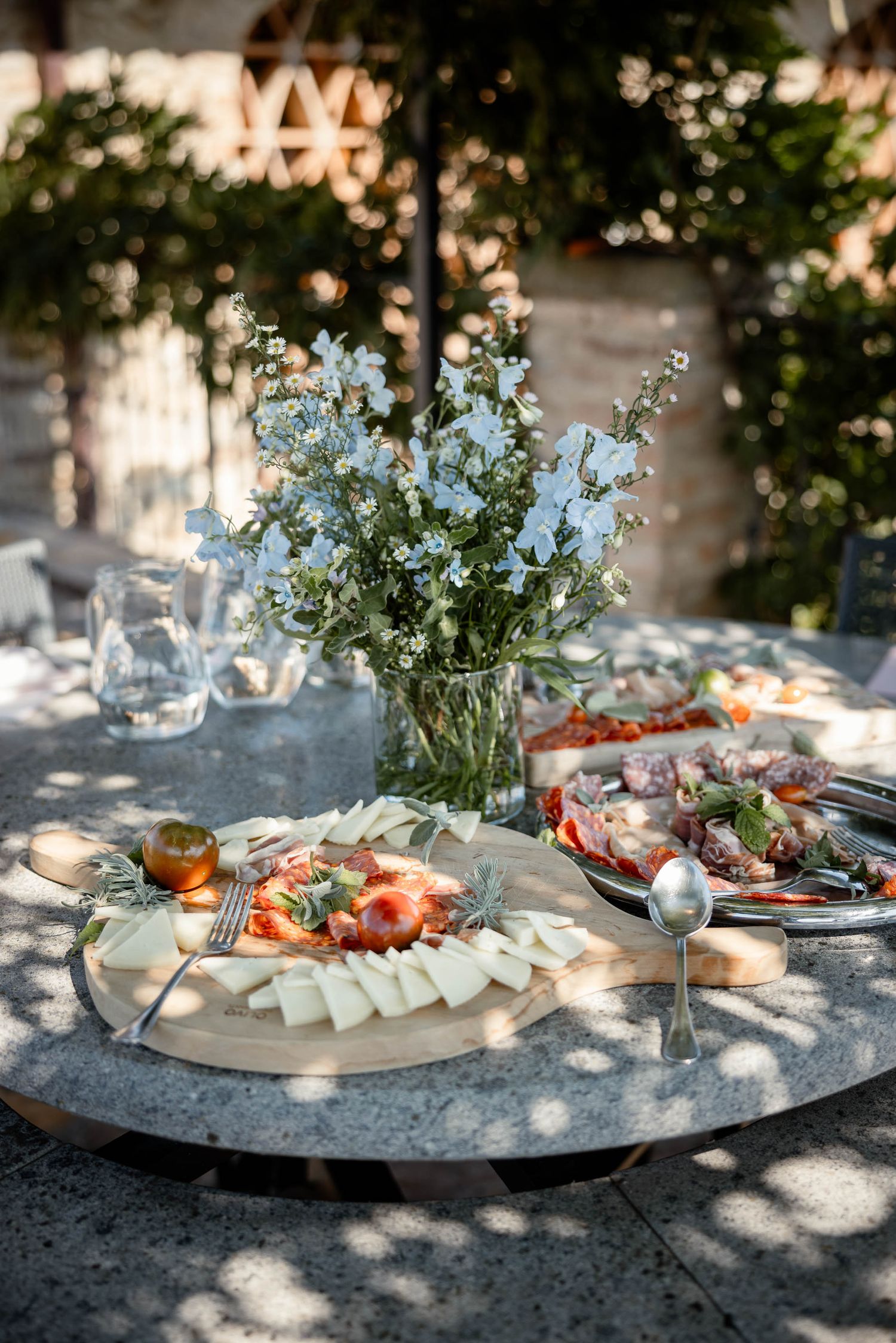 Elegant outdoor table setting with floral centerpiece and charcuterie platter.