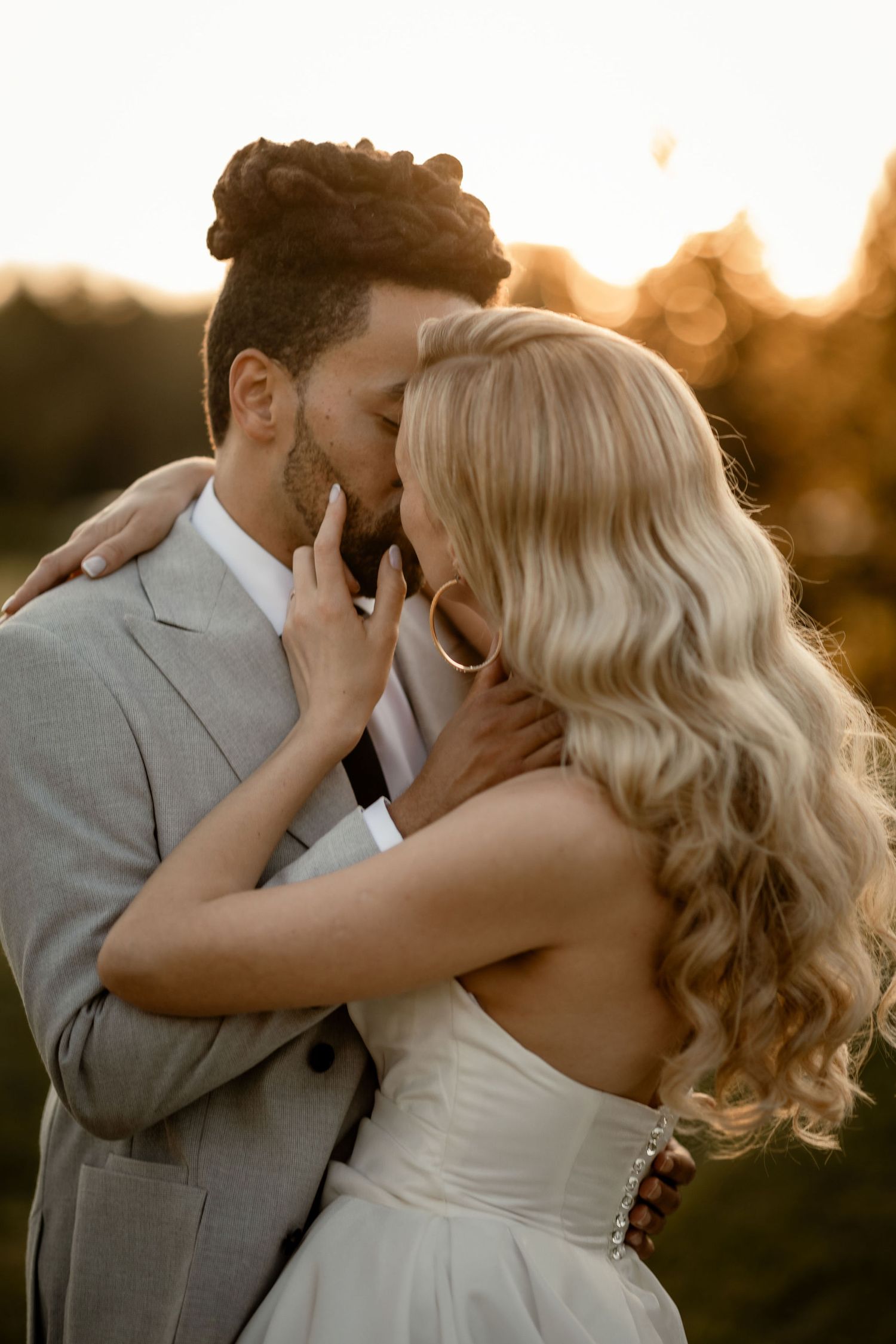 A romantic couple embraces intimately during golden hour sunset in formal wedding attire.