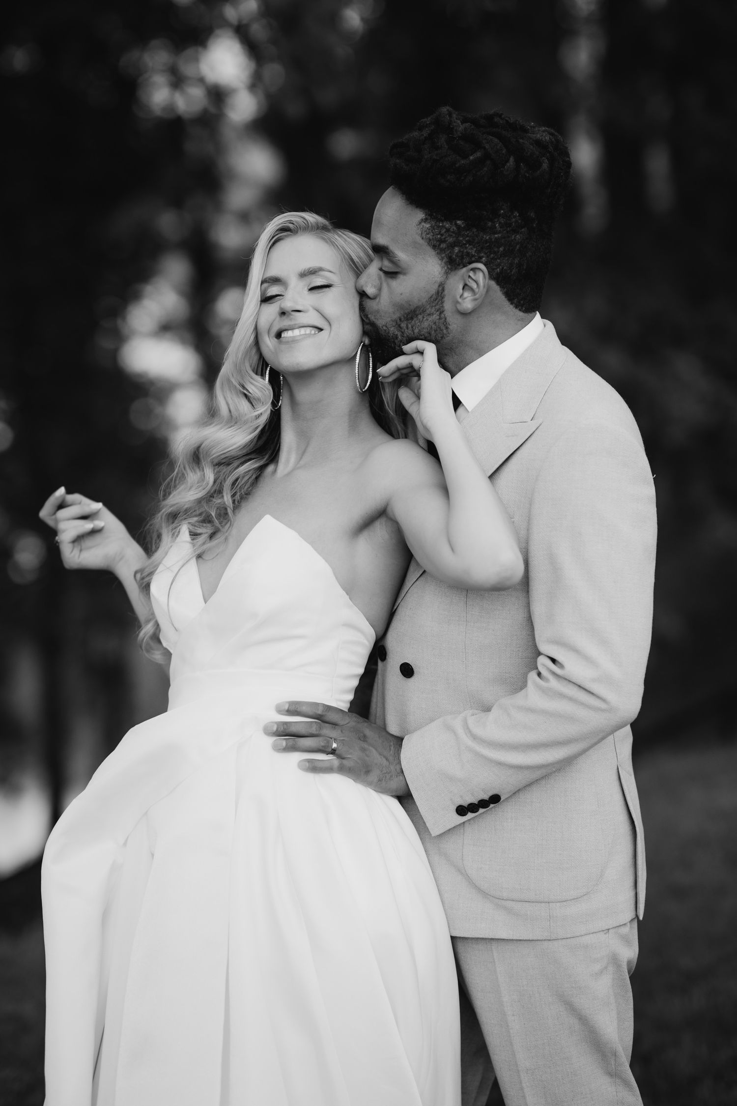 A romantic black and white photo of a wedding couple sharing an intimate moment in formal attire outdoors.