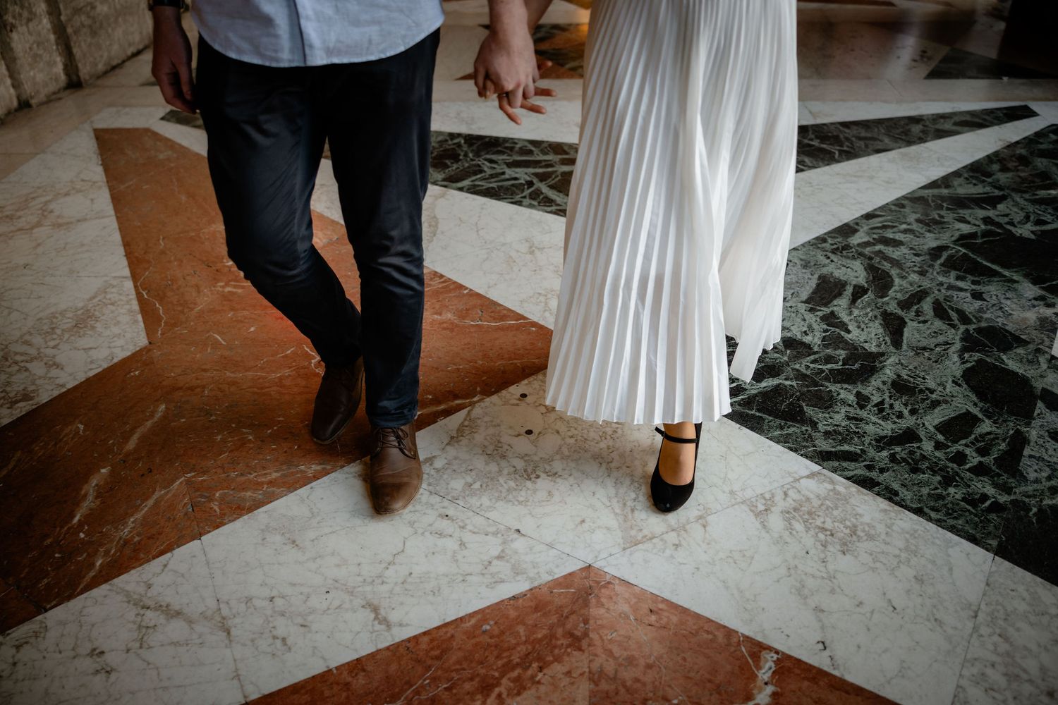 Close-up of couple standing on marble floor showing contrasting dress shoes and formal attire from waist down.