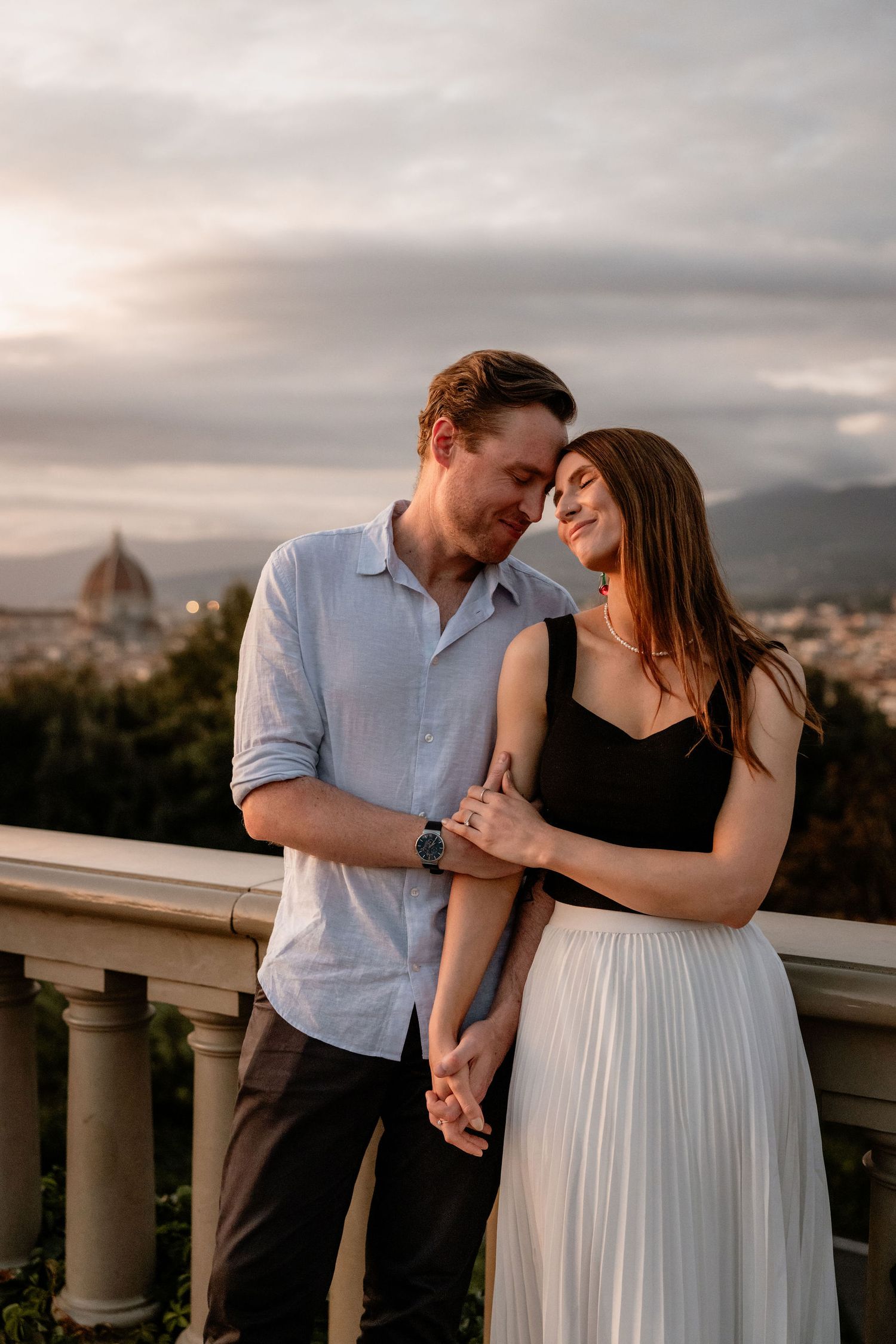 Romantic couple embrace on an overlook in Florence with the iconic Duomo cathedral in the background at sunset.