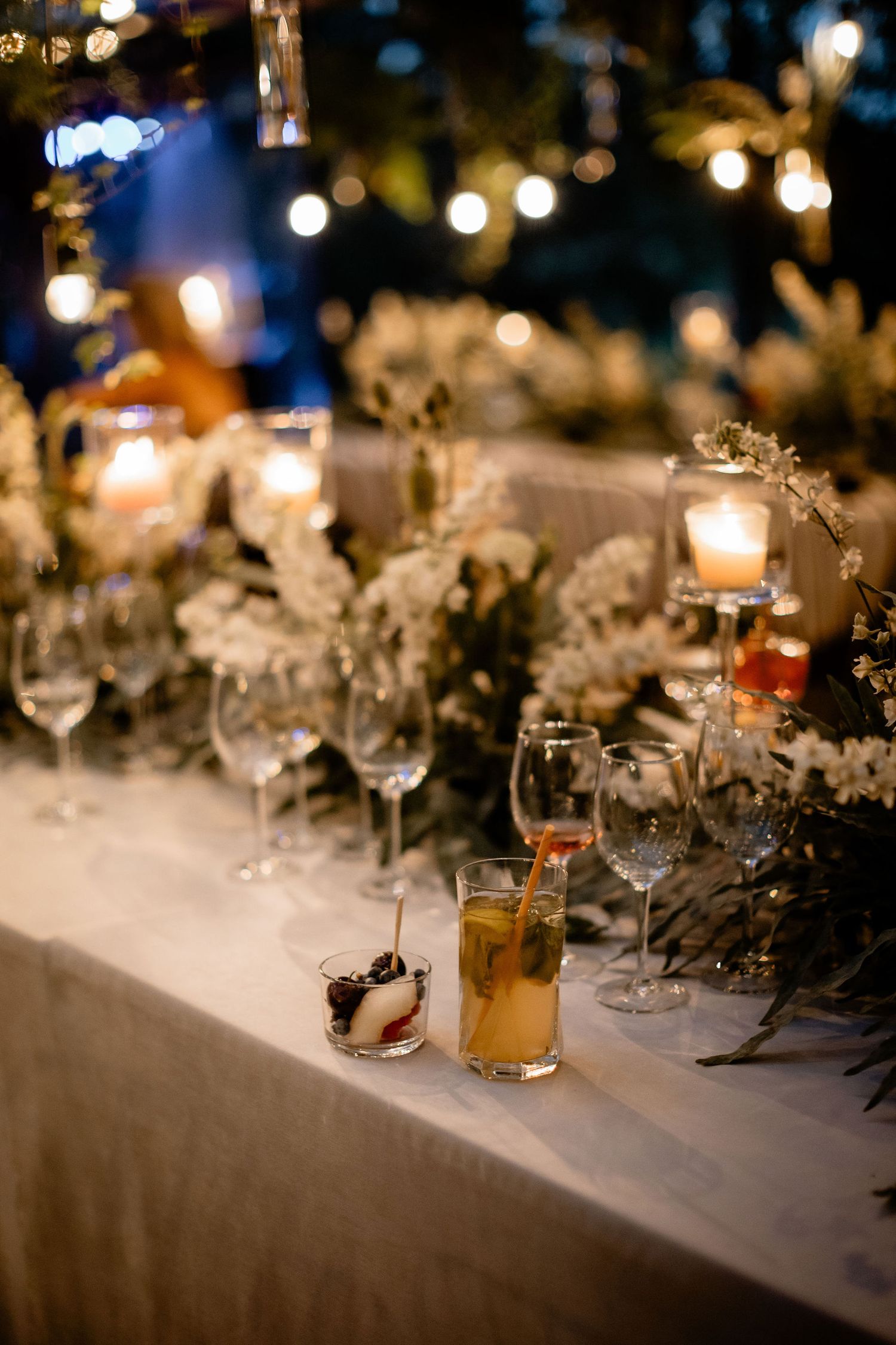 Elegant wedding reception table setting with candlelight, wine glasses and floral decorations at dusk.