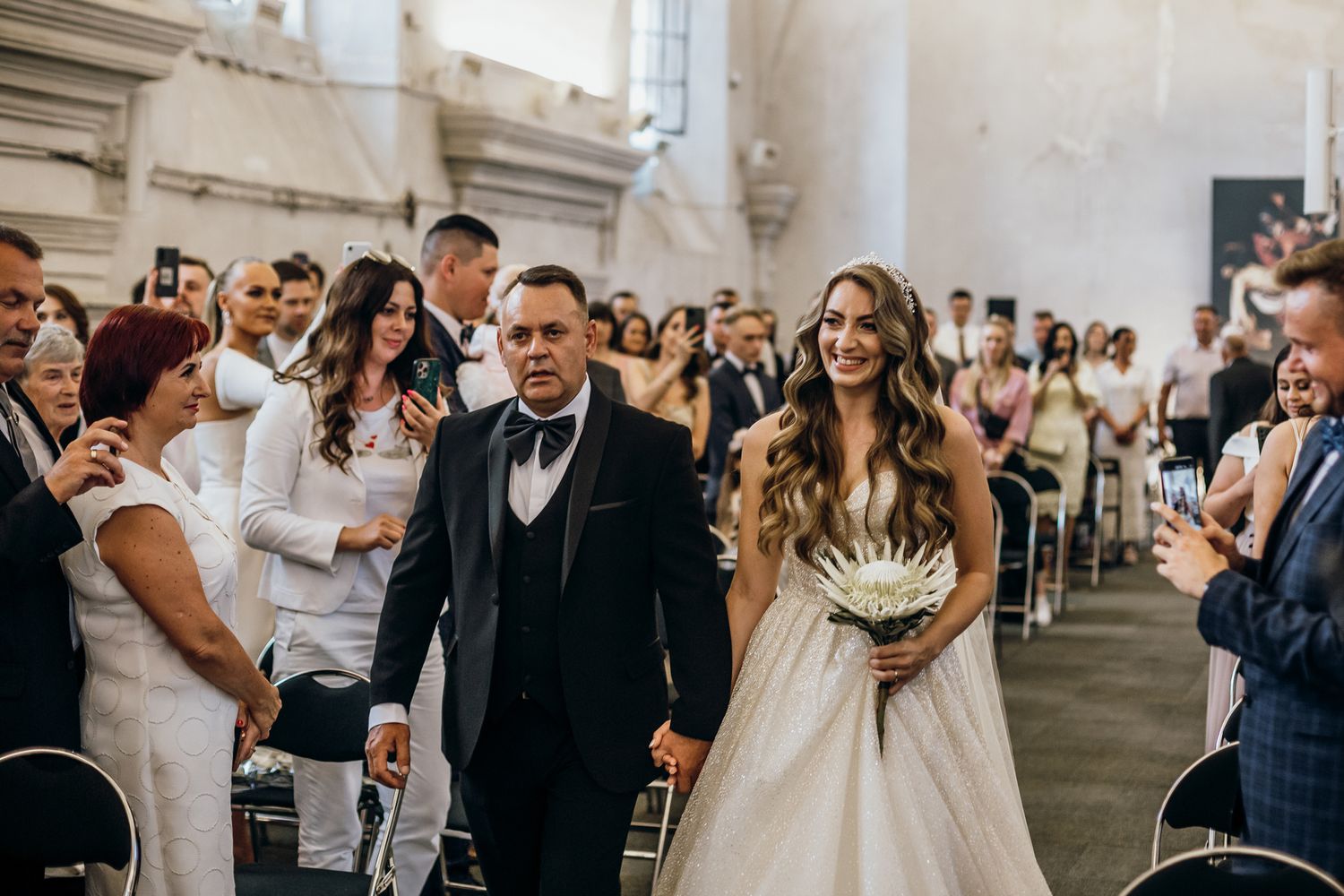 Wedding guests gather in a bright industrial venue space during a celebration ceremony.