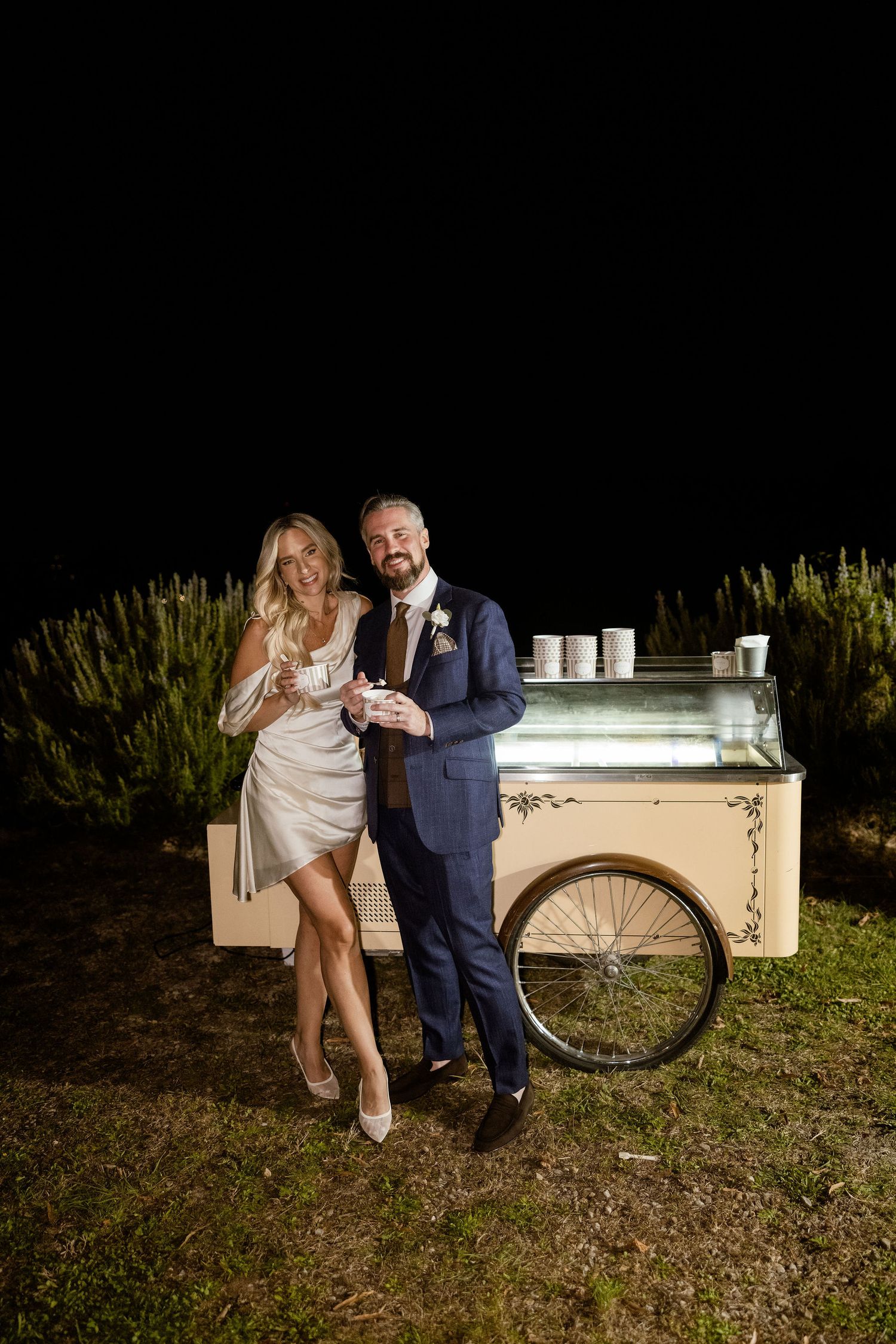 A couple shares a romantic moment on a vintage white bench in an outdoor garden setting.