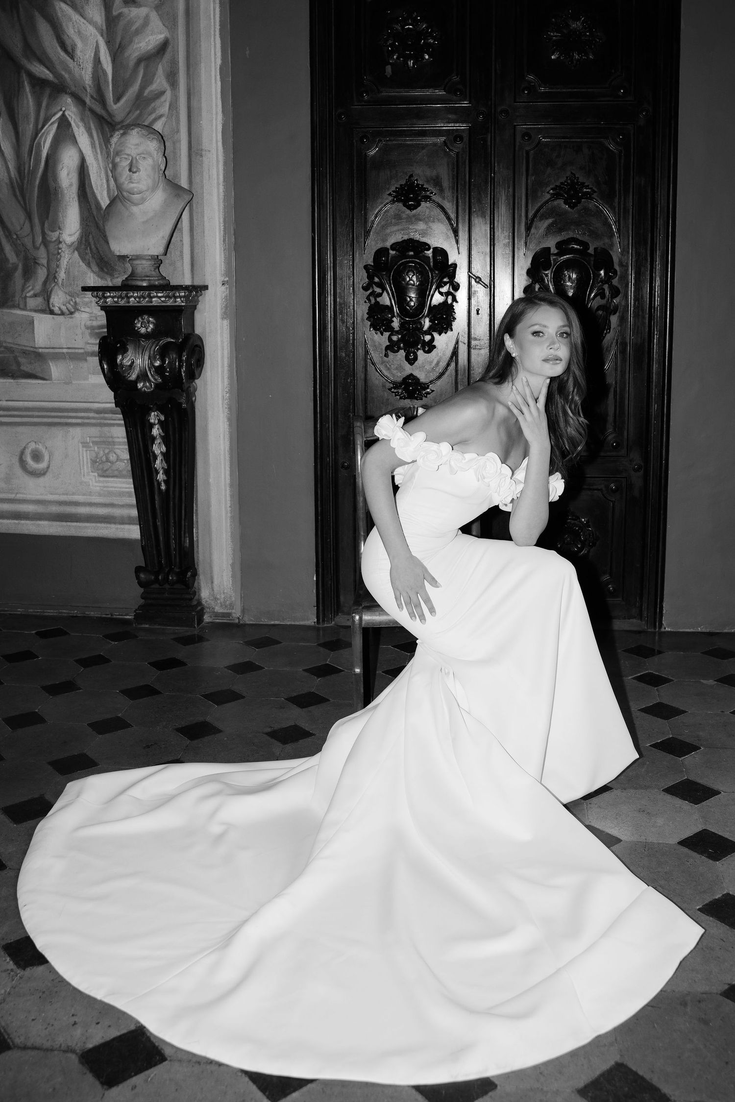 Elegant bride in white strapless gown with flowing train poses in ornate room with black and white decor and marble floors.