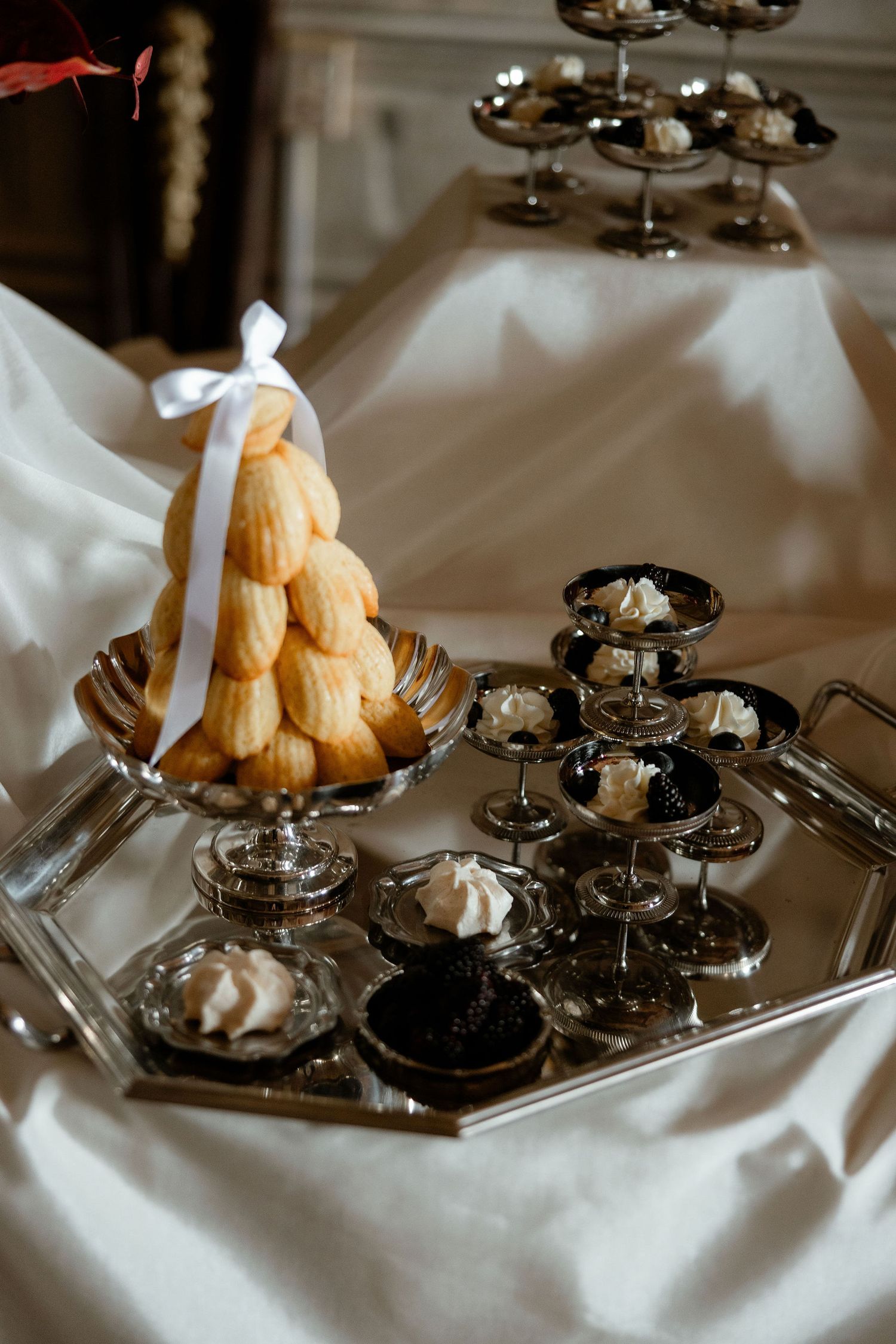 Vintage silver tea service set arranged elegantly on white linen tablecloth with decorative metallic and glass elements.