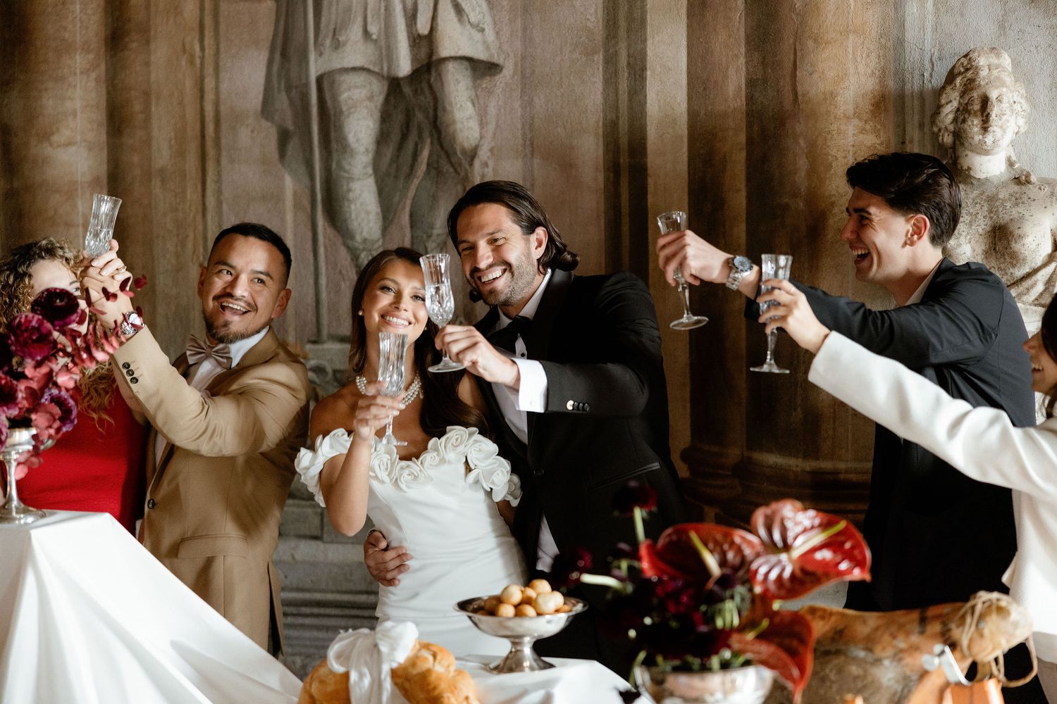 Wedding guests laughing and celebrating together at a festive reception table with floral decorations and food.