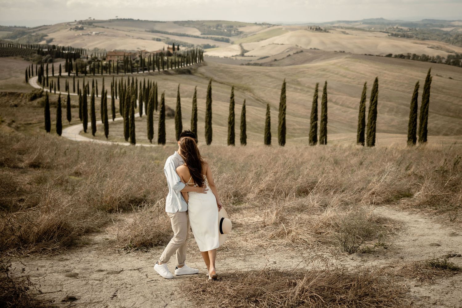 Couple walking through rolling hills with cypress trees in Italian countryside.