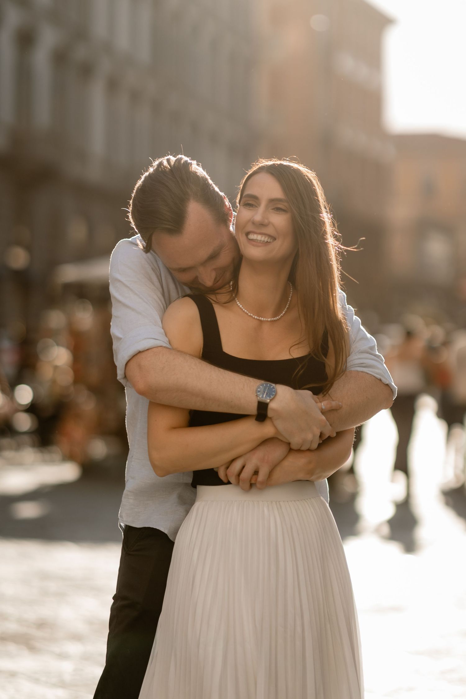 A tender moment between a couple in casual attire hugging and smiling in golden sunlight.