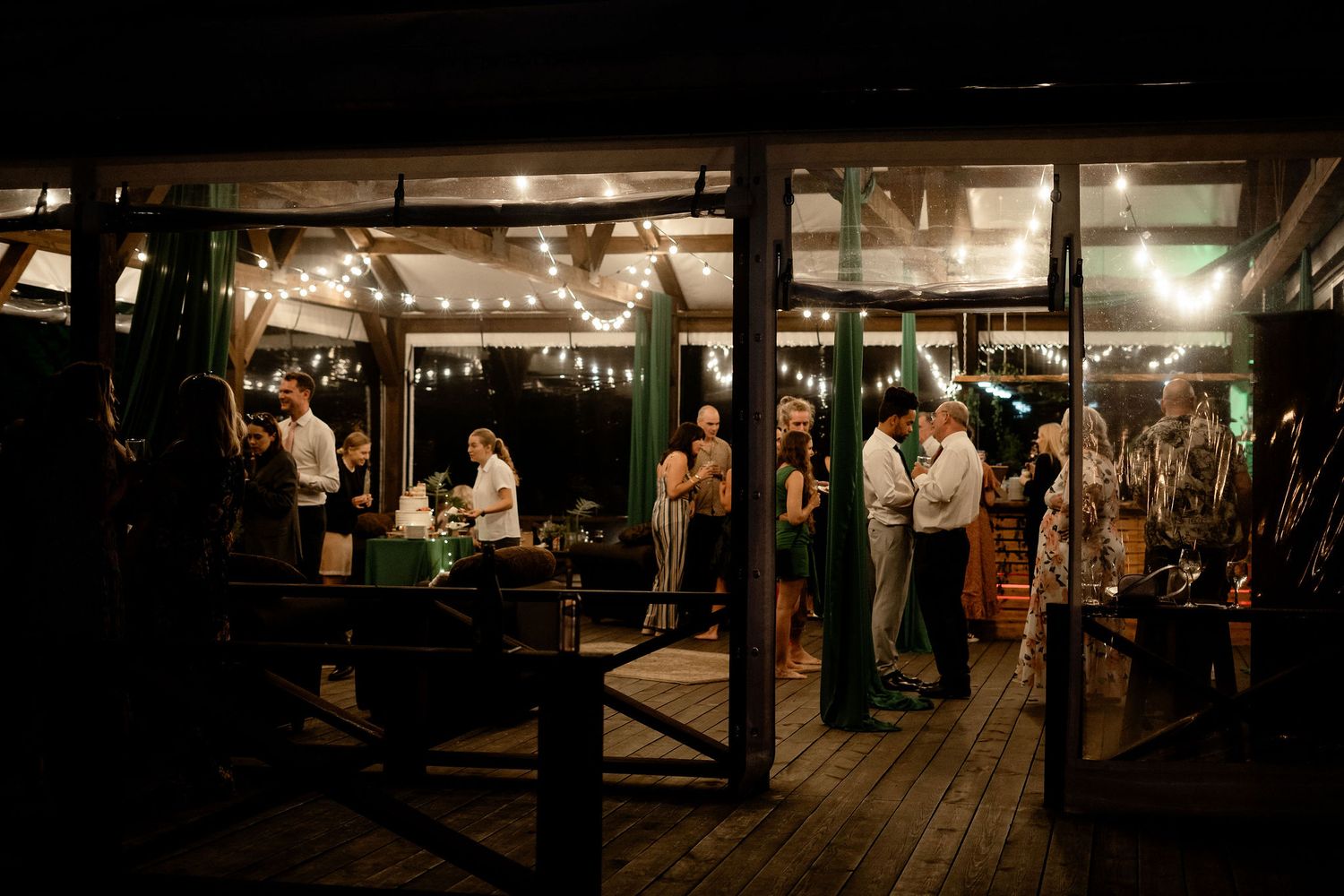 People dancing and mingling at a rustic evening celebration with string lights on a wooden deck.