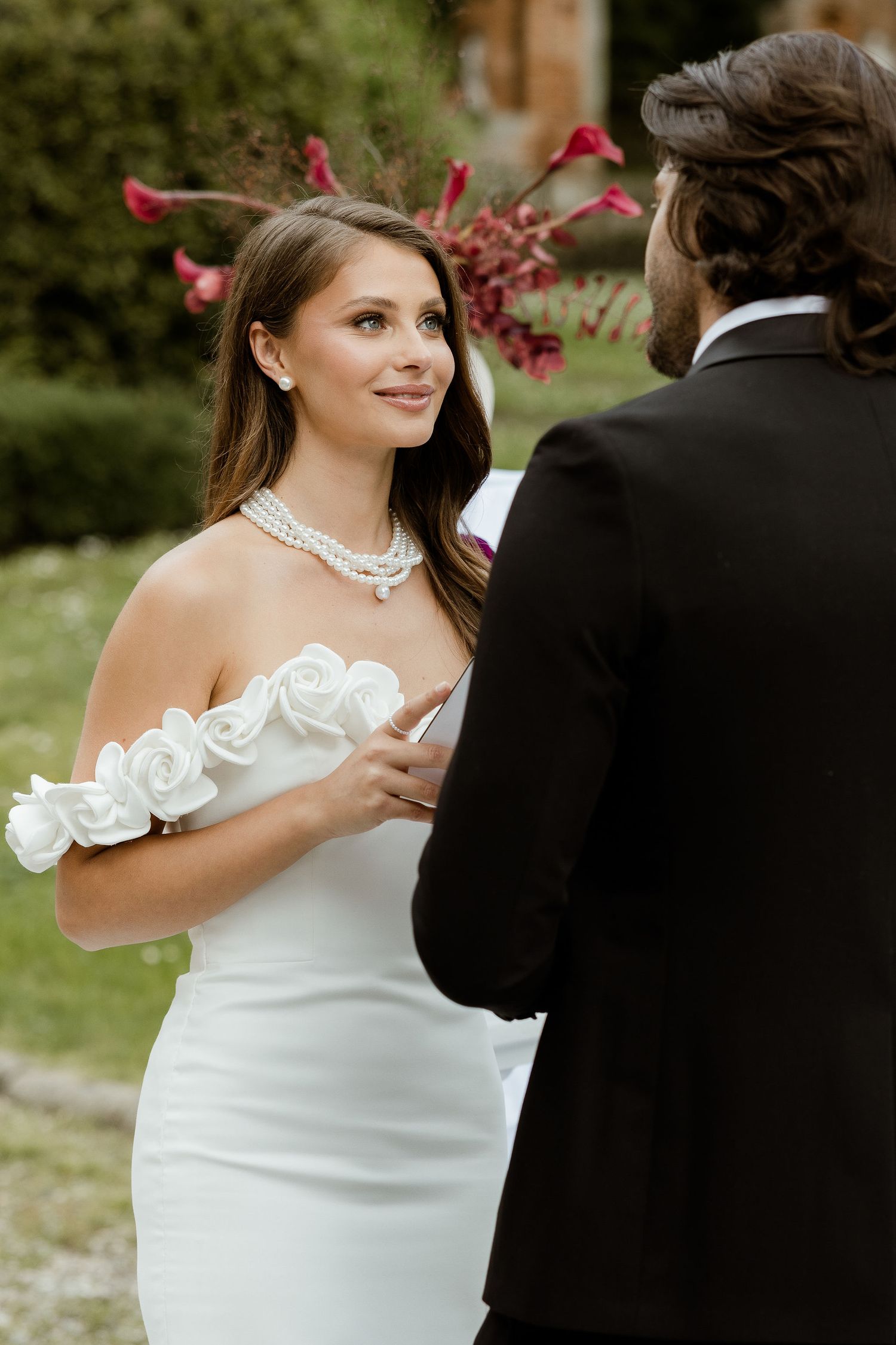 Wedding couple shares a romantic dance moment in matching white and black attire amid garden scenery.