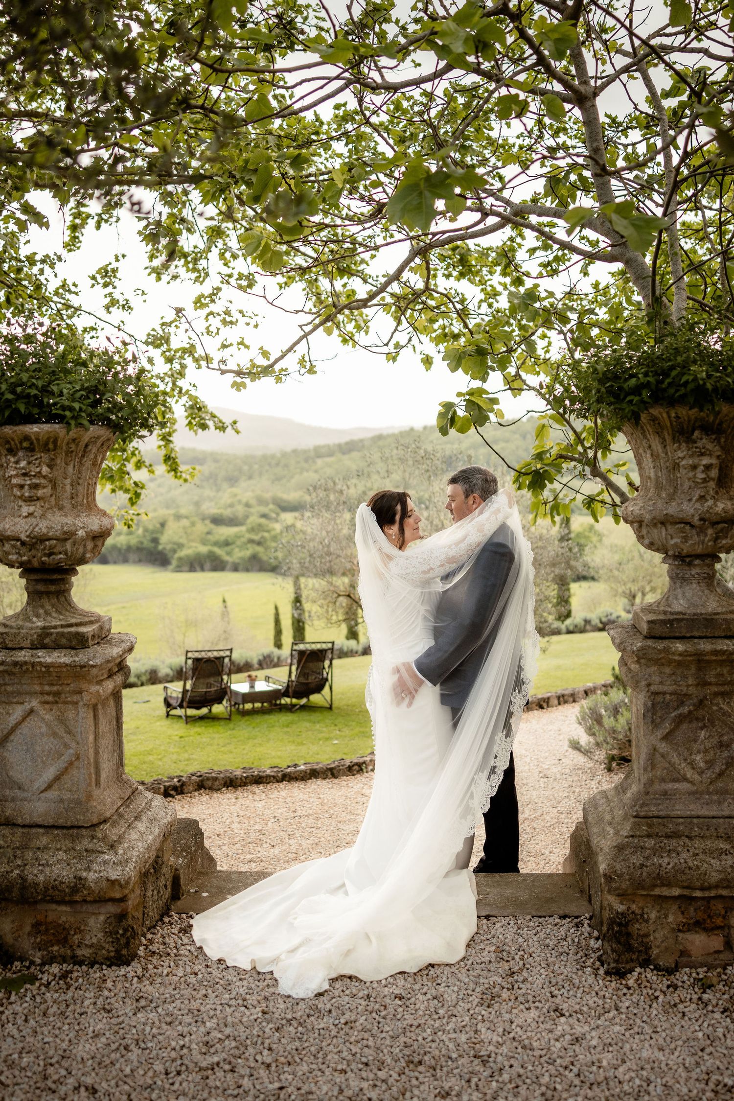 Elegant garden wedding moment framed by stone urns and greenery overlooking a scenic countryside landscape.