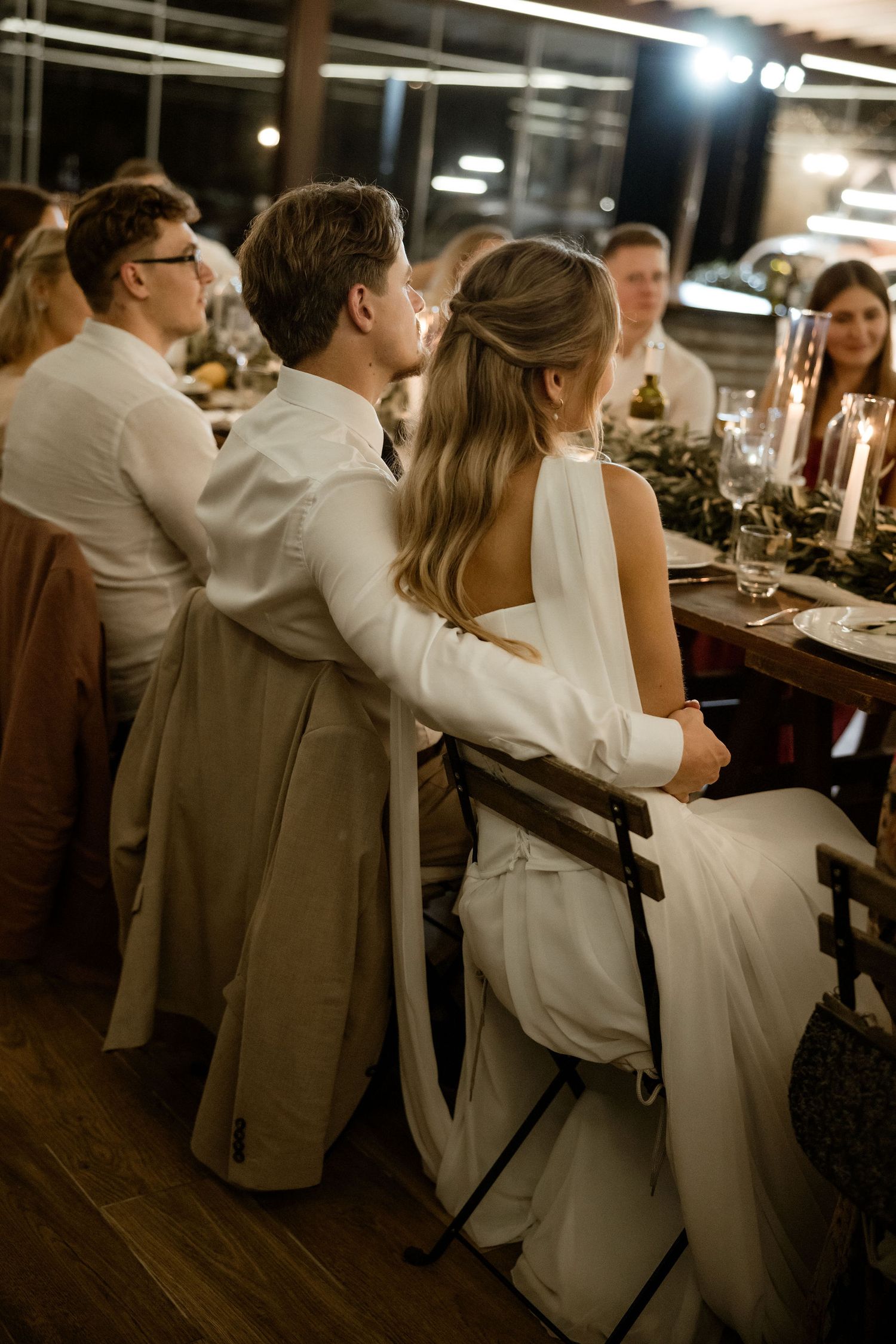 Wedding guests seated at a long dinner table enjoying an intimate reception in warm ambient lighting.