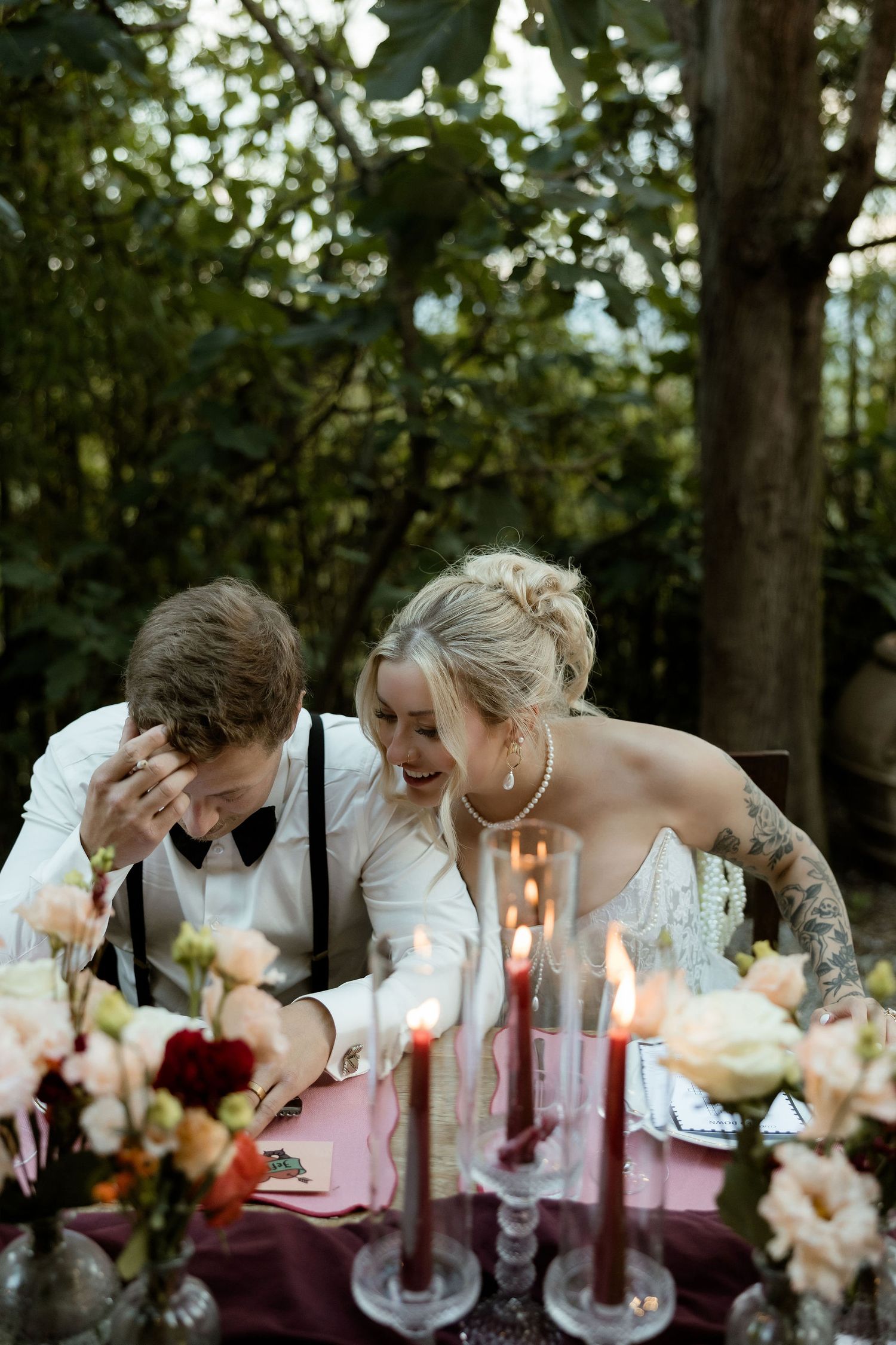 A candlelit wedding reception table with guests leaning in close together for an intimate moment during dinner.