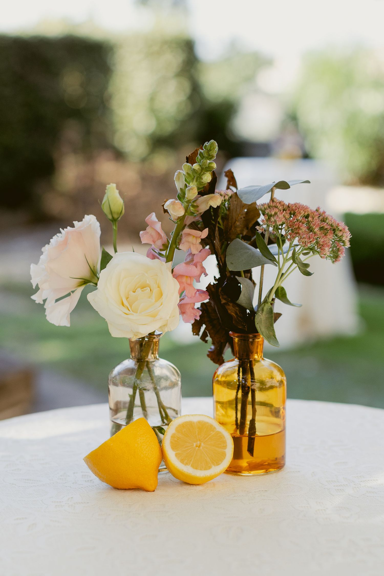 Small glass vases with delicate pink flowers and fresh citrus fruits create an elegant table centerpiece display.