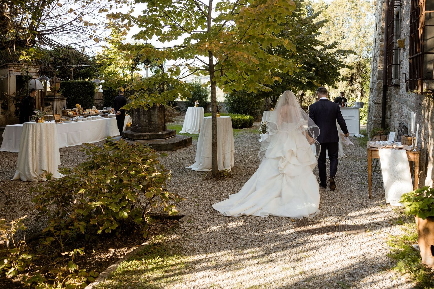 Elegant outdoor wedding ceremony setup with white chairs and floral arrangements along a tree-lined path in autumn.